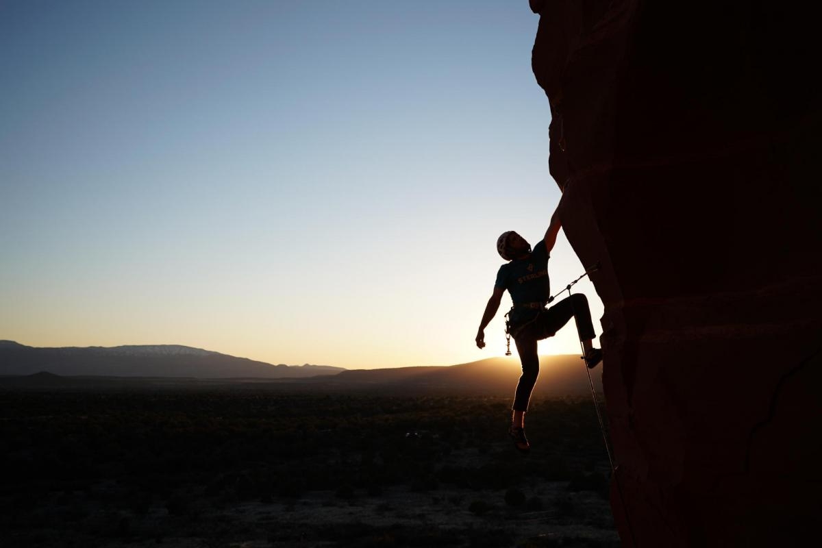 Climber roped to cliff, both silhouetted against sky