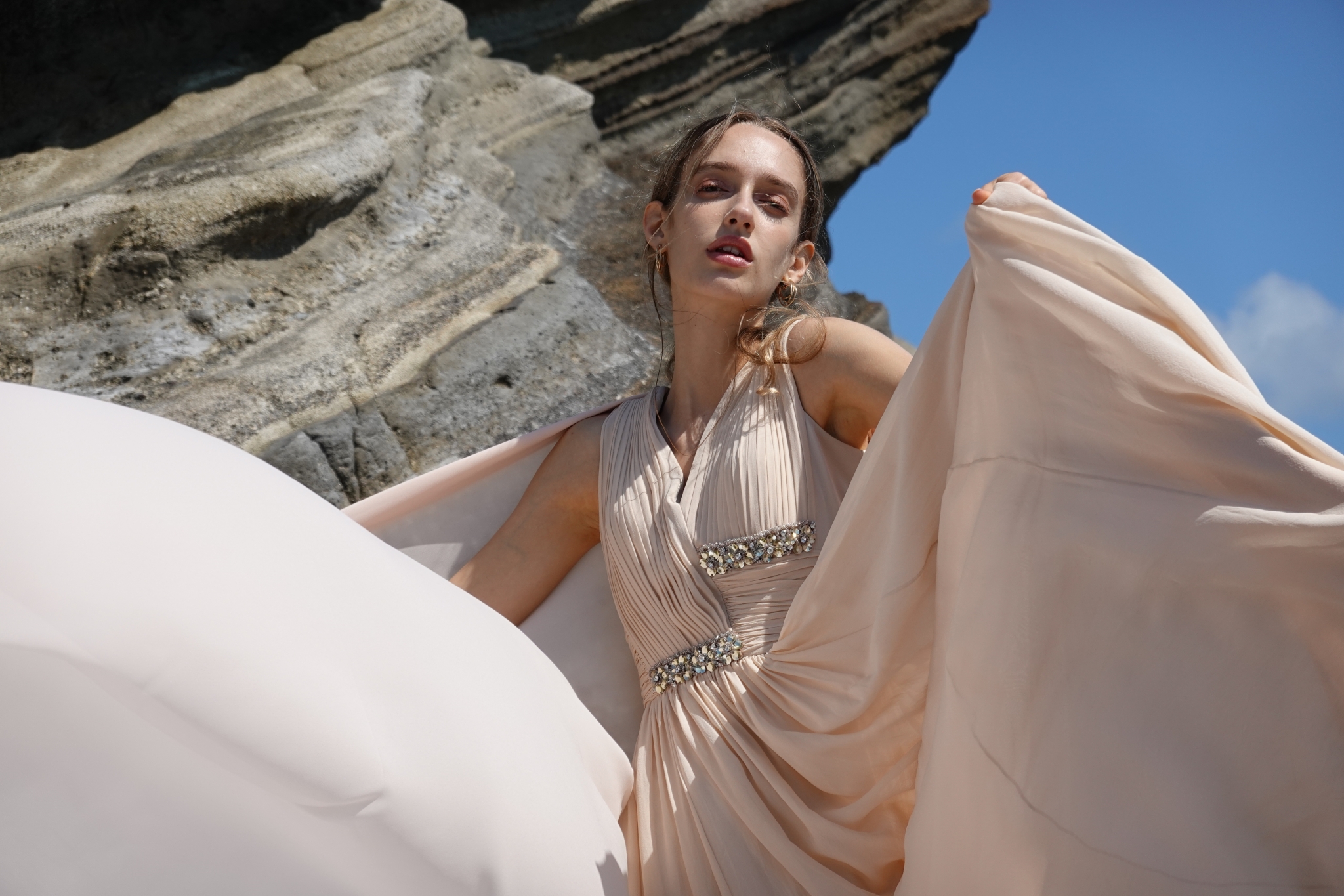 Female model sat in long silk dress with rocky outcrop in background