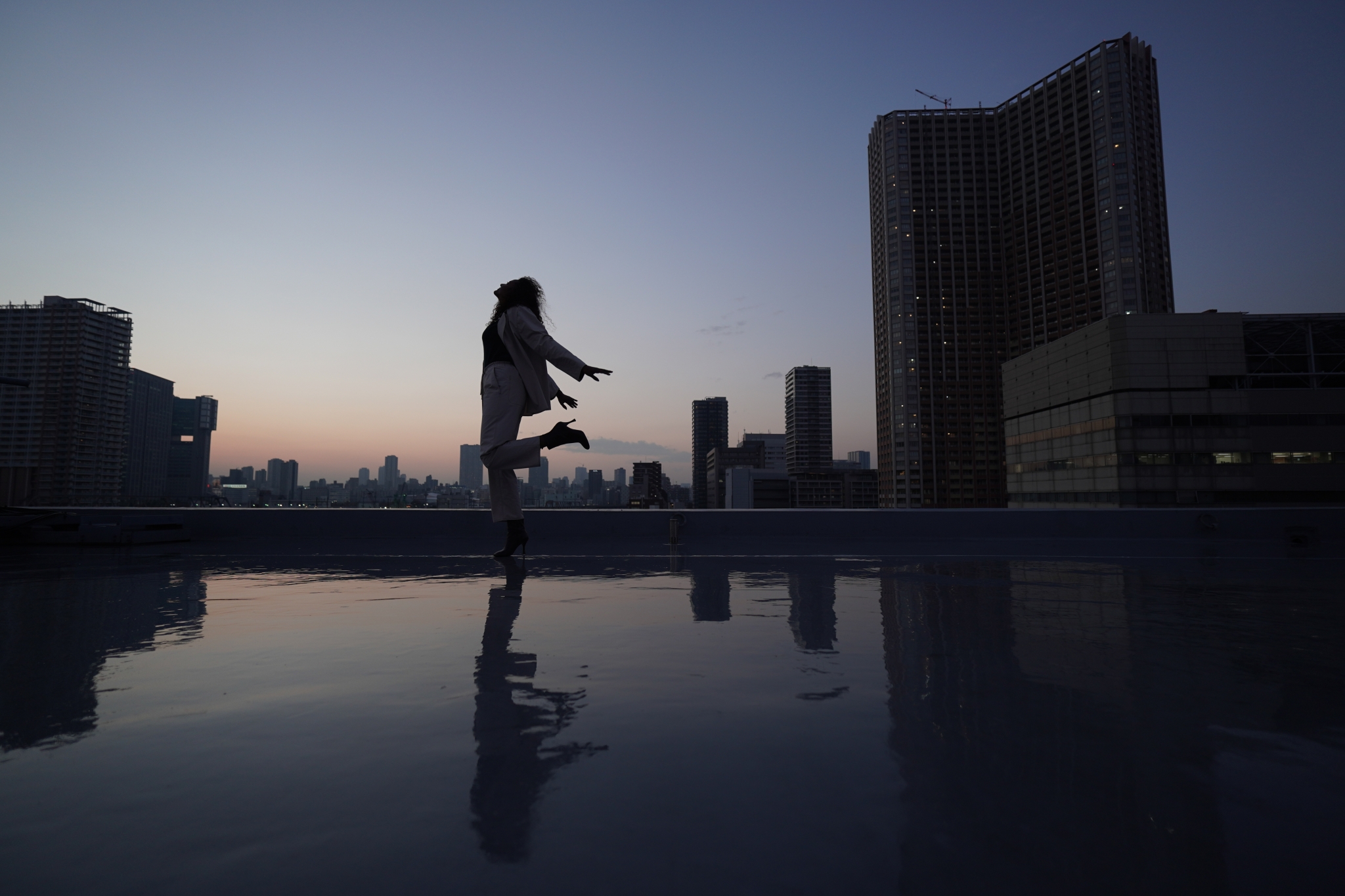 Female dancer at dusk by water in an urban setting, silhouetted against the sky 