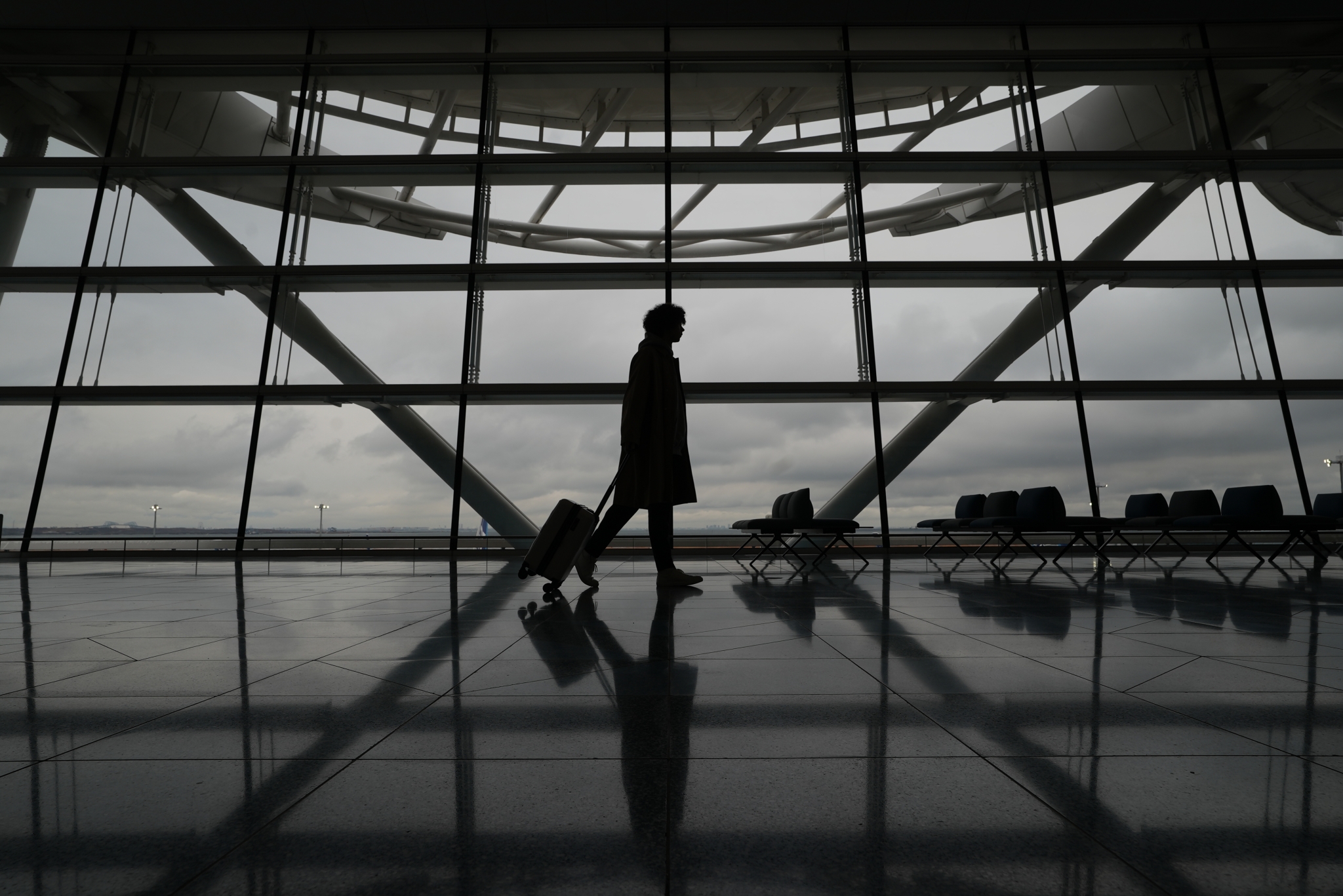 Silhouette of a person wheeling a suitcase through a large glass airport