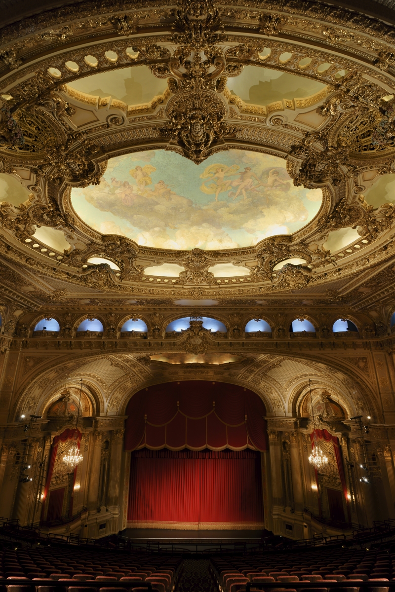 Proscenium arch and red curtain in theatre, with ornate ceiling decoration and murals