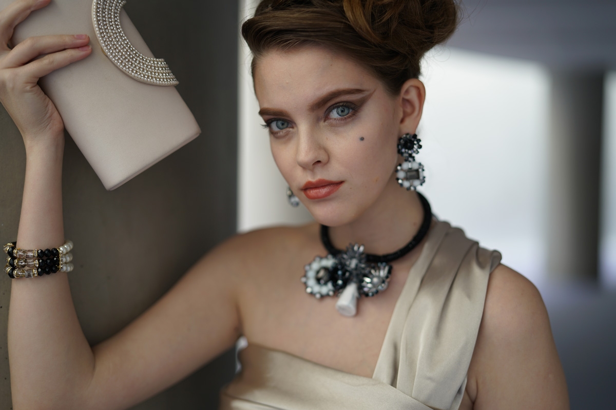 Female model with neck and ear jewellery, holding purse up and looking toward the camera