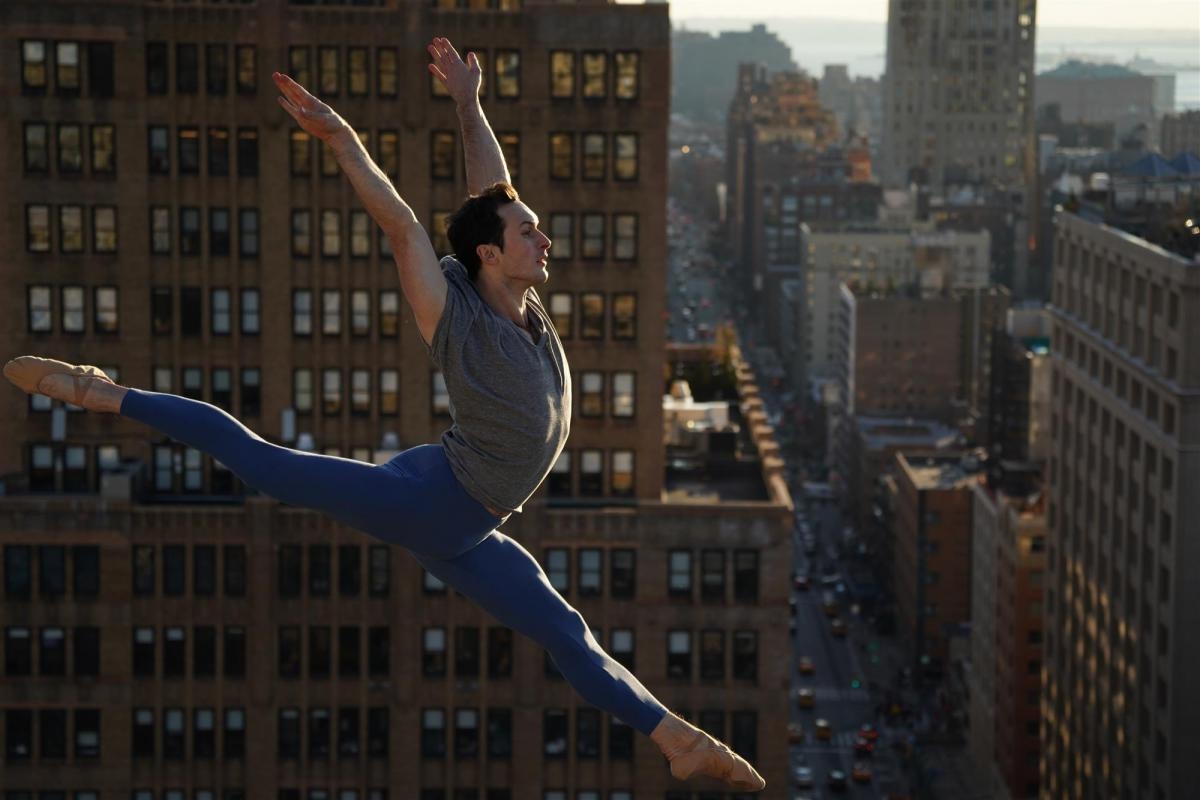 Man performing balletic jump against rooftop cityscape