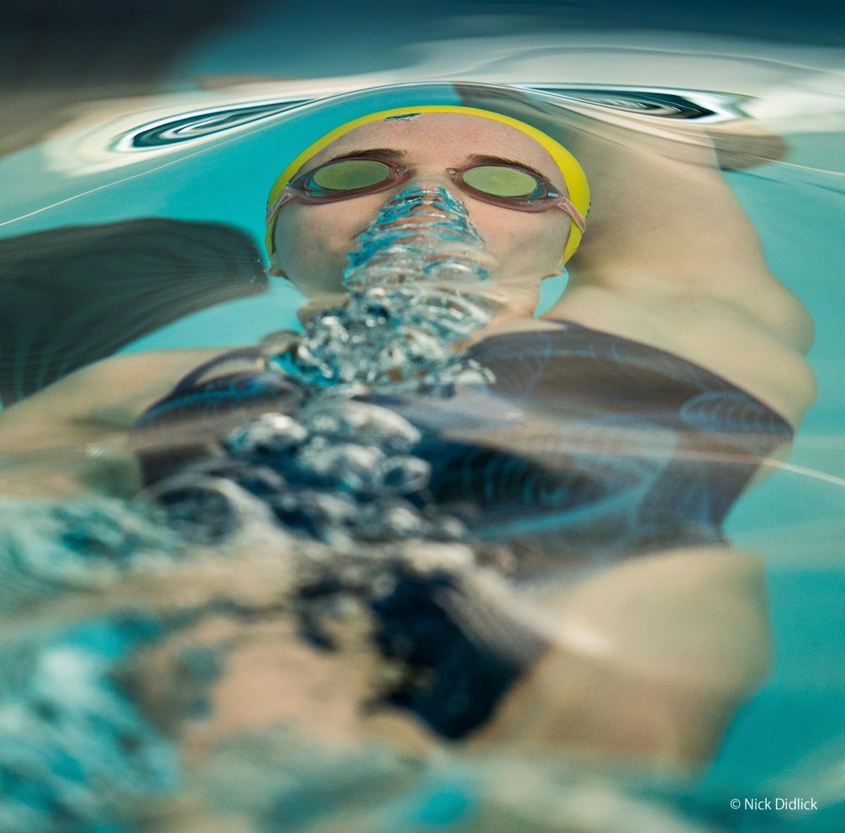 Backstroke swimmer under water with goggles and stream of bubbles from nose
