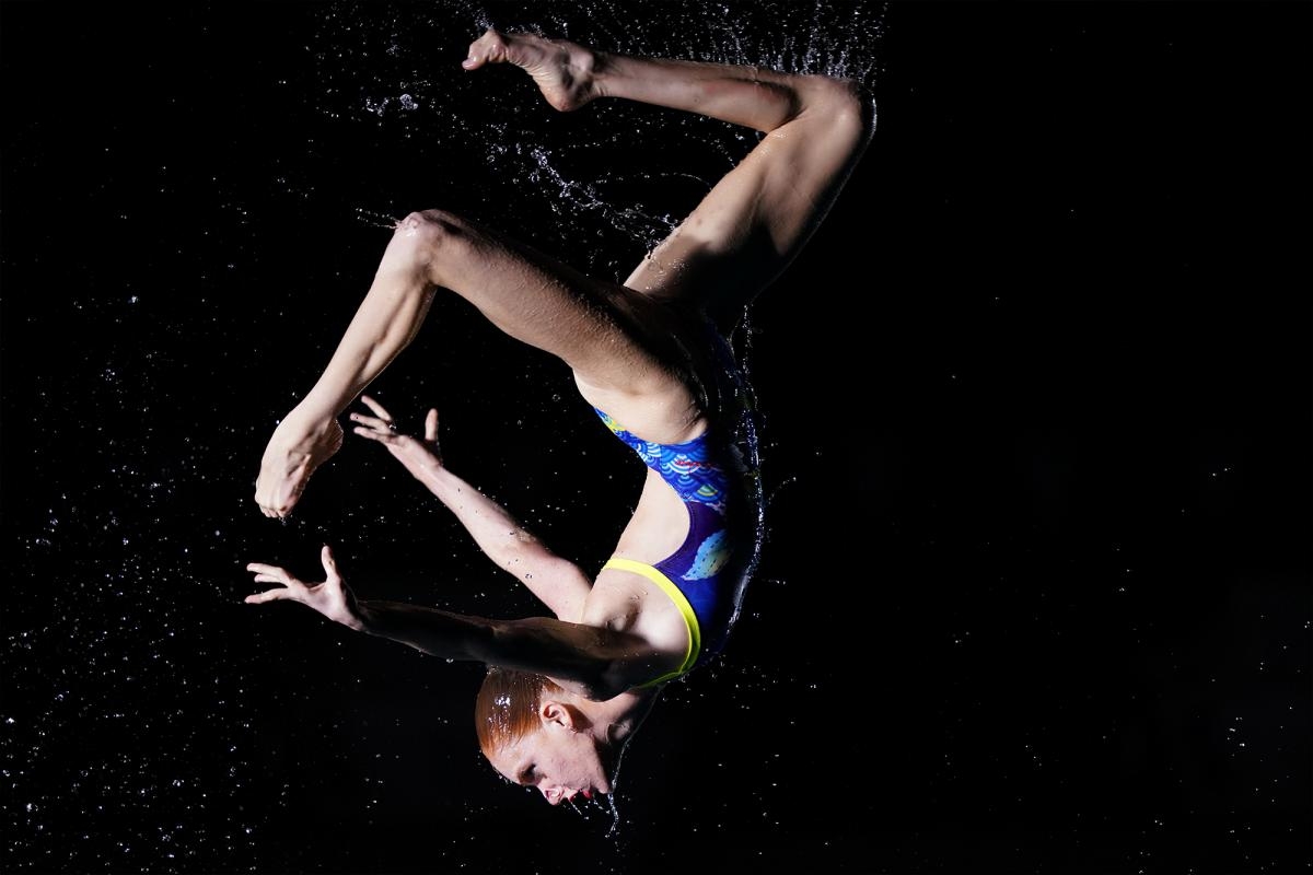 Synchronised swimmer in mid-somersault surrounded with water droplets