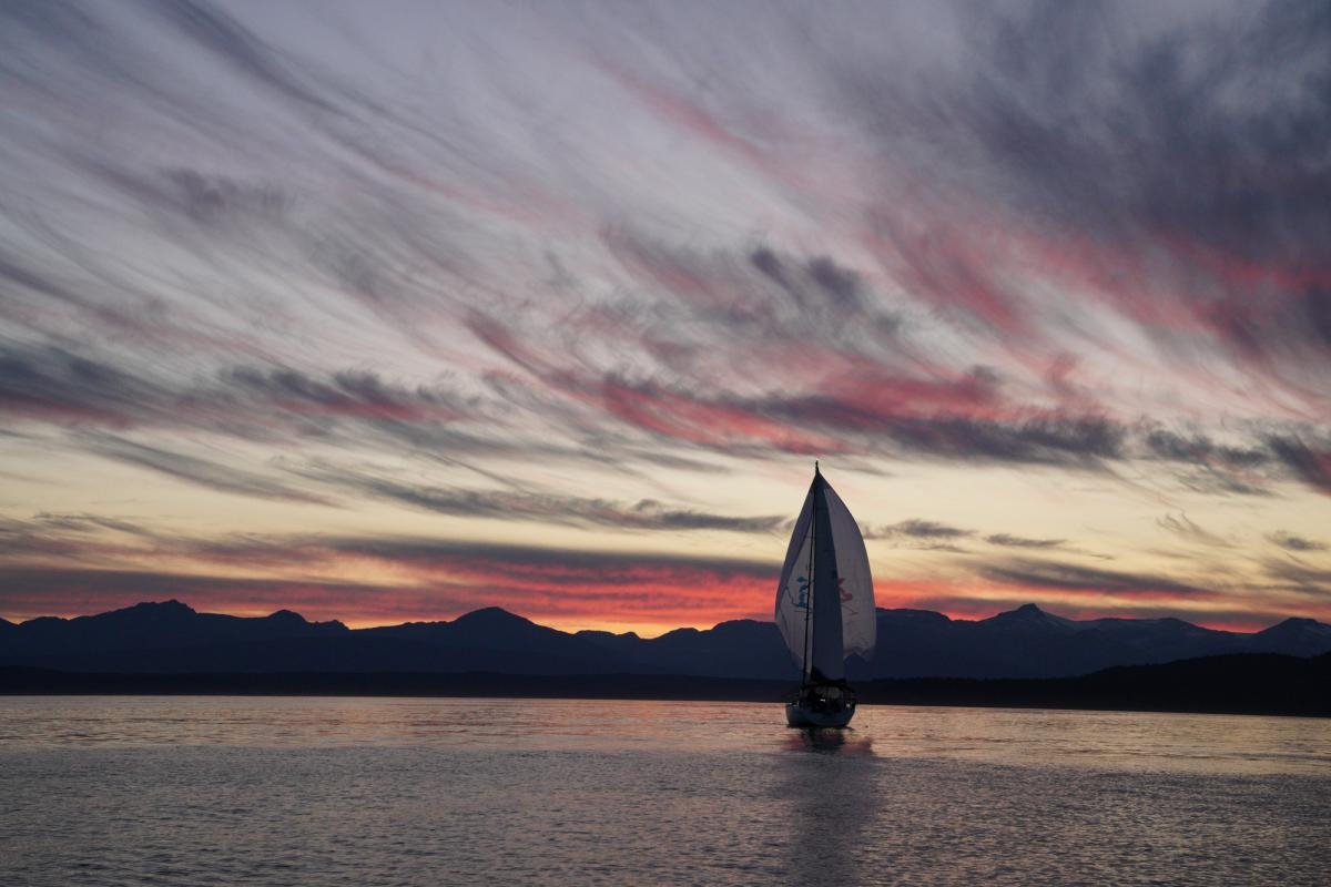 Landscape of a sailing boat crossing water as the sun set behind mountains in the background