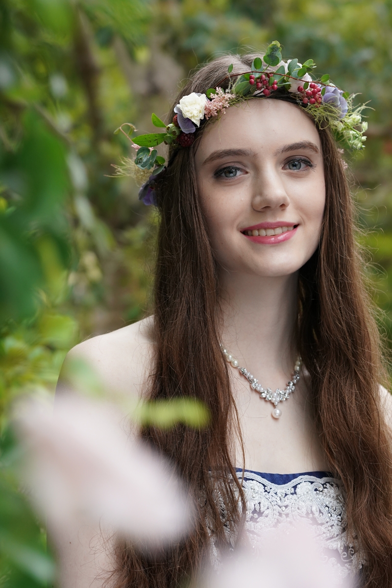 Portrait of female model wearing a garland of flowers with greenery in a bokeh background