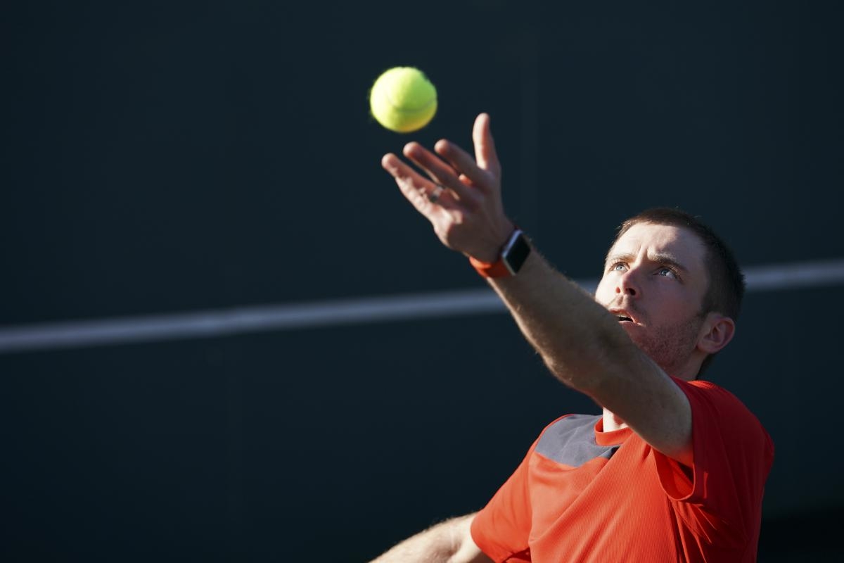 Portrait of male tennis player throwing a tennis ball in the air, before taking an opening shot