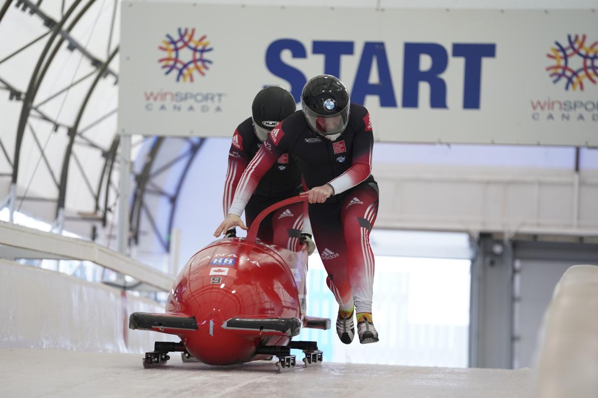 Two bobsledders push a red bobsleigh at the start of a race