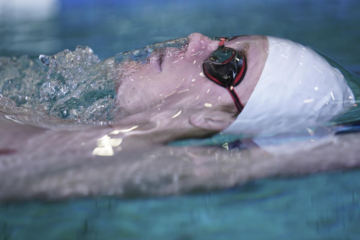 Close-up of male swimmer in water, doing backstroke