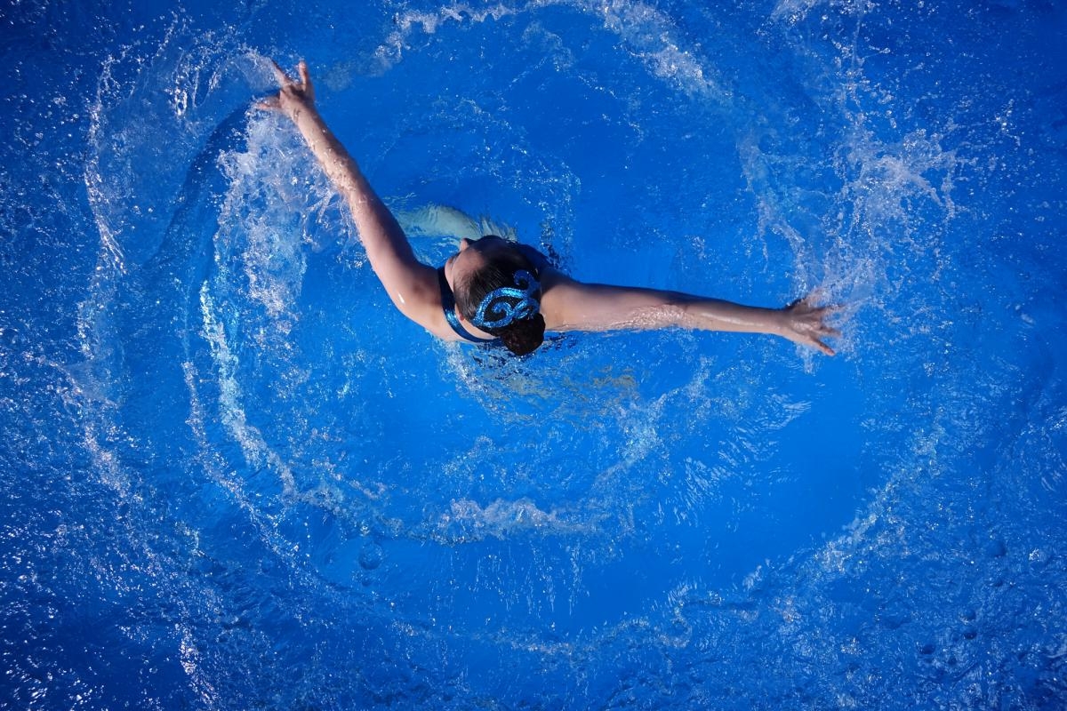 Aerial shot of female artistic swimmer in water, arms outstretched