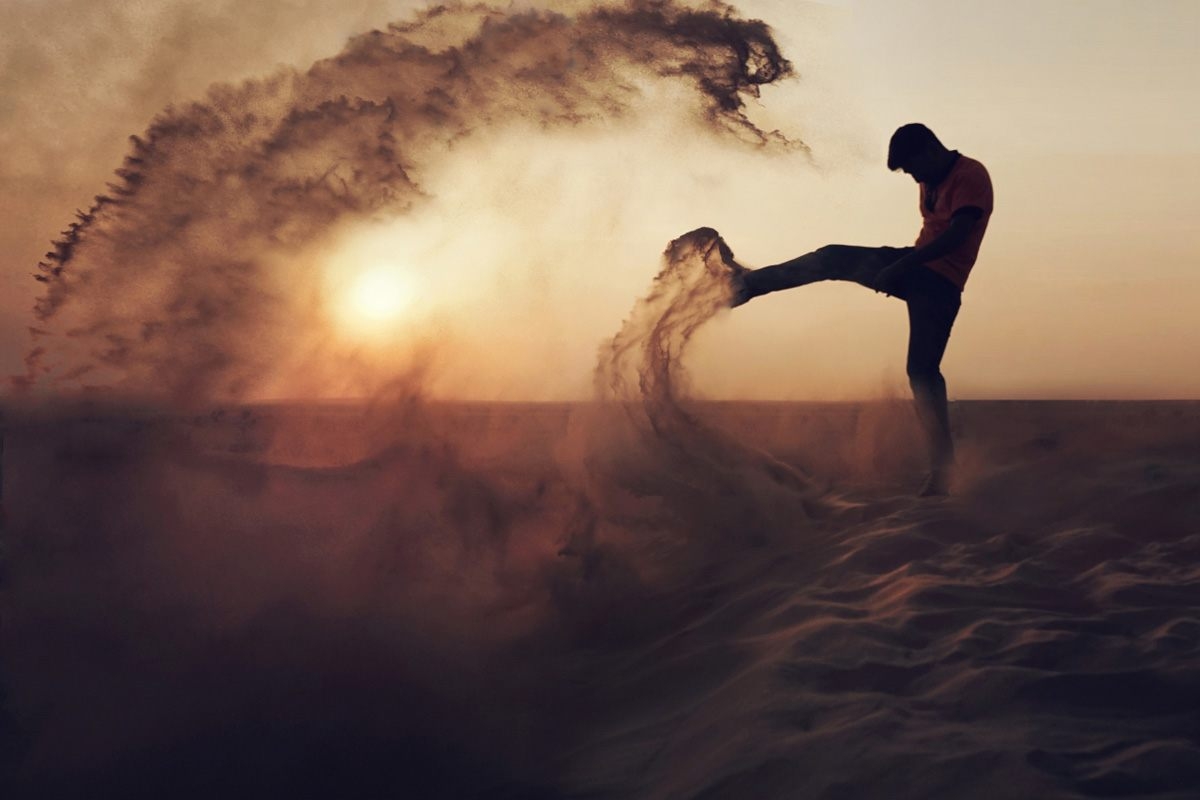 Man kicking up a huge plume of sand, silhouetted against the sun