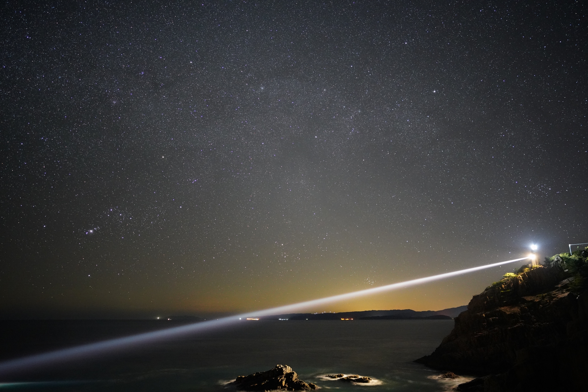Night-time landscape of a beam of light streaming from a lighthouse on a cliff