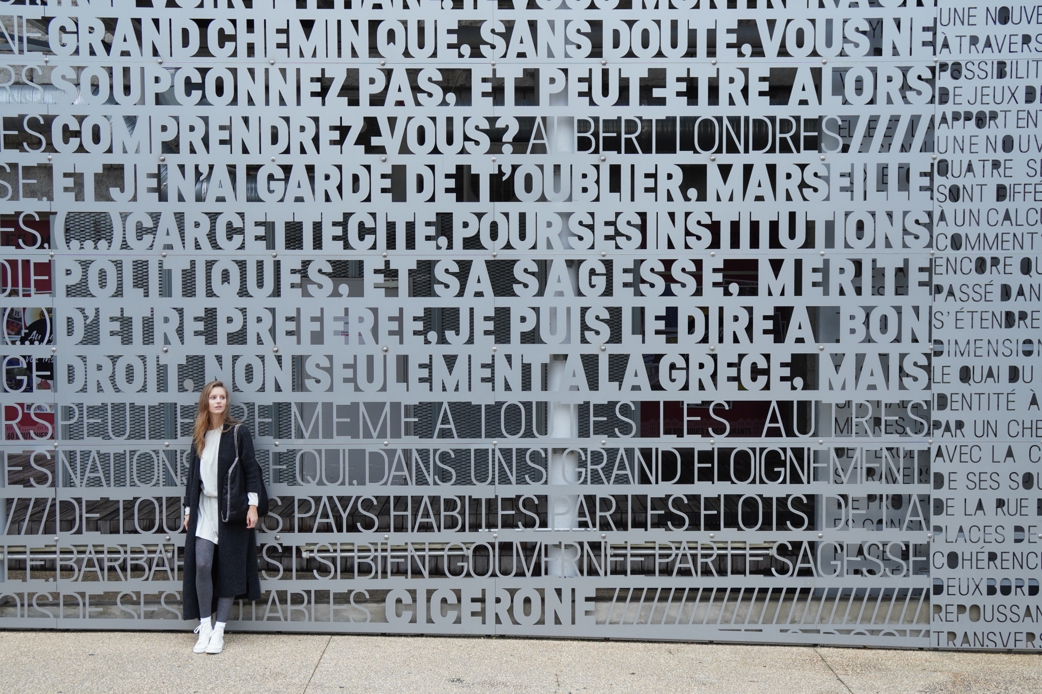 Wide shot of woman standing by a wall inscribed with French text