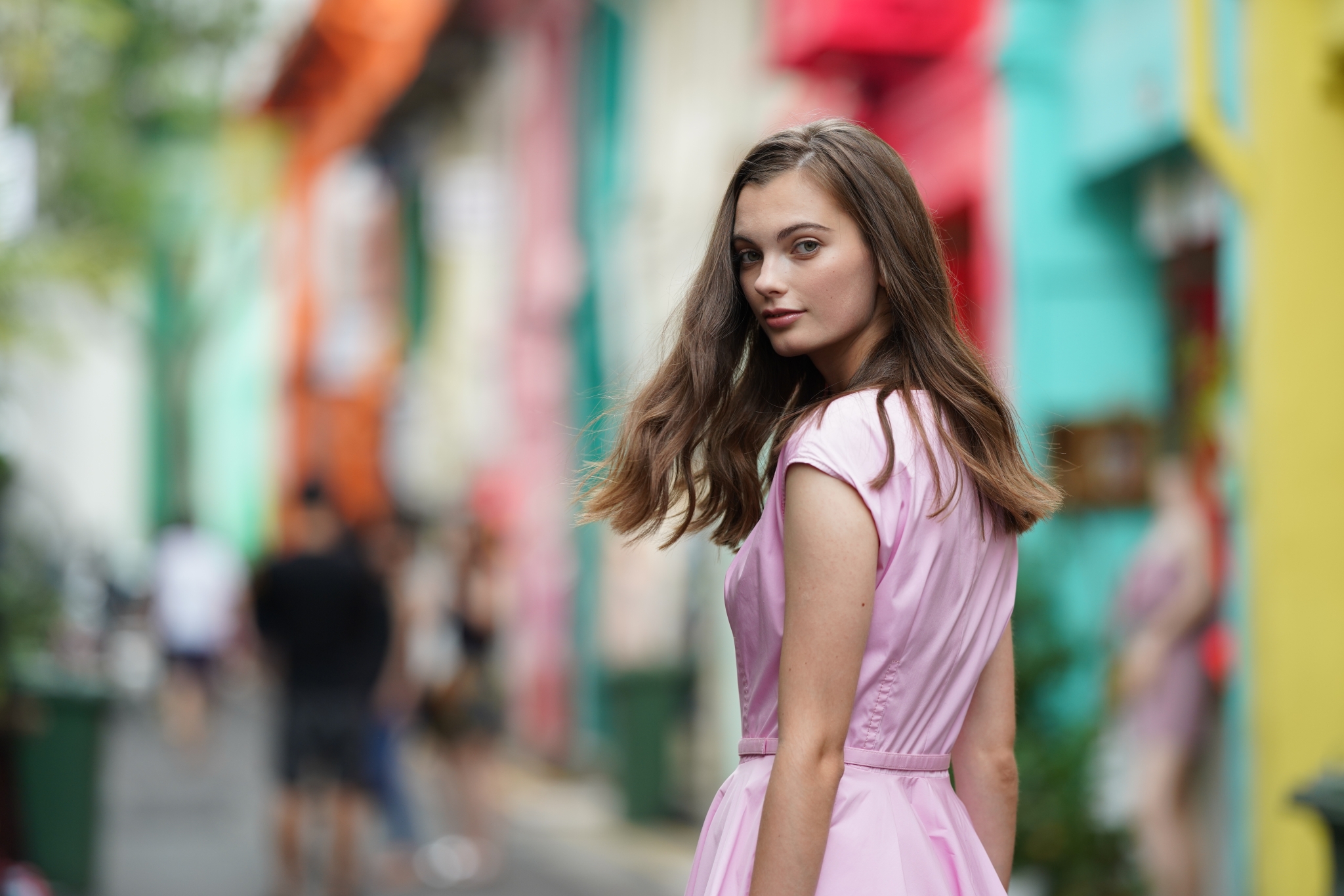 Female model looking over shoulder towards camera with colourful houses in a bokeh background
