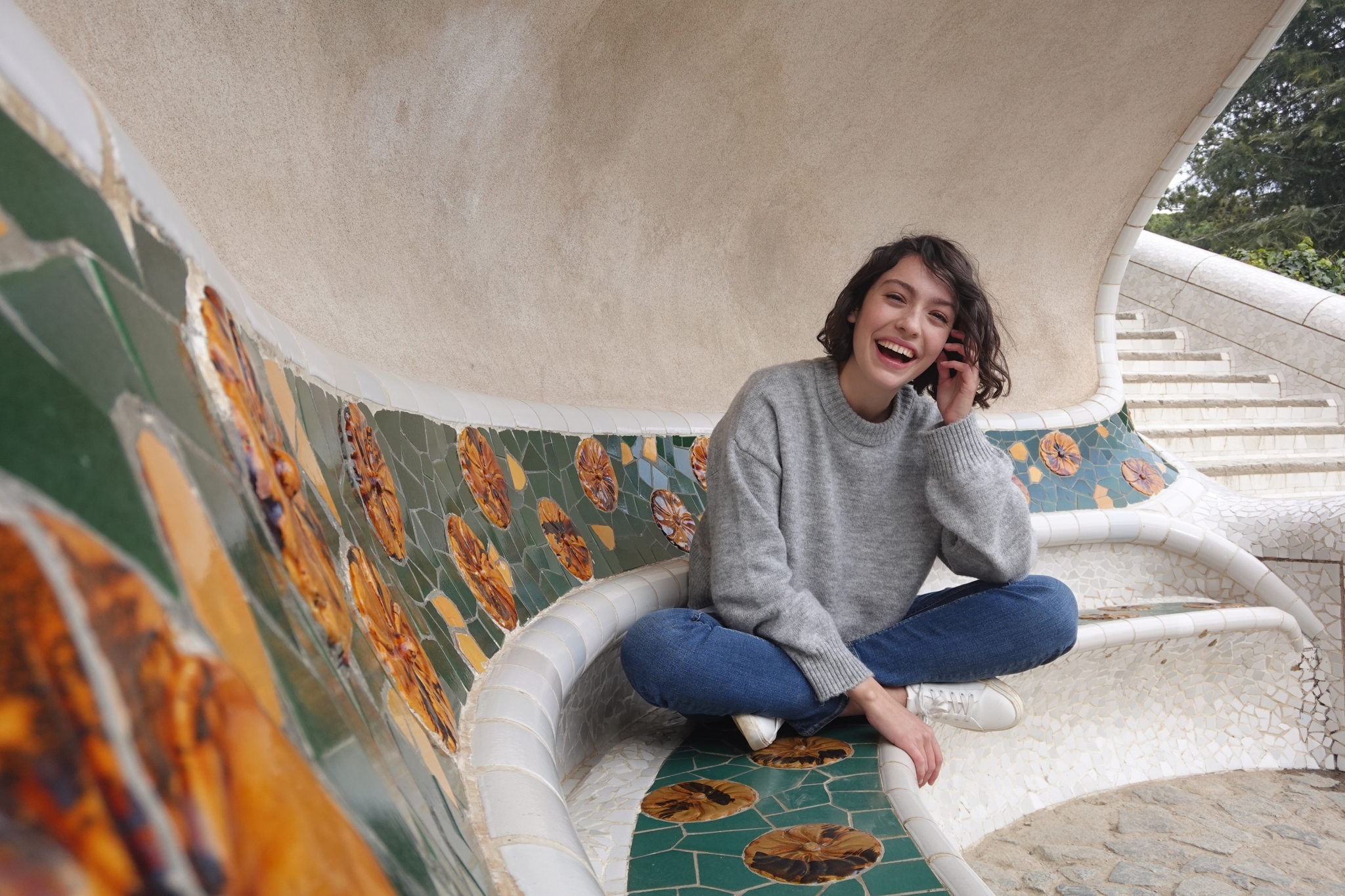 Female model sat on a white stone curved bench with colourful tiles