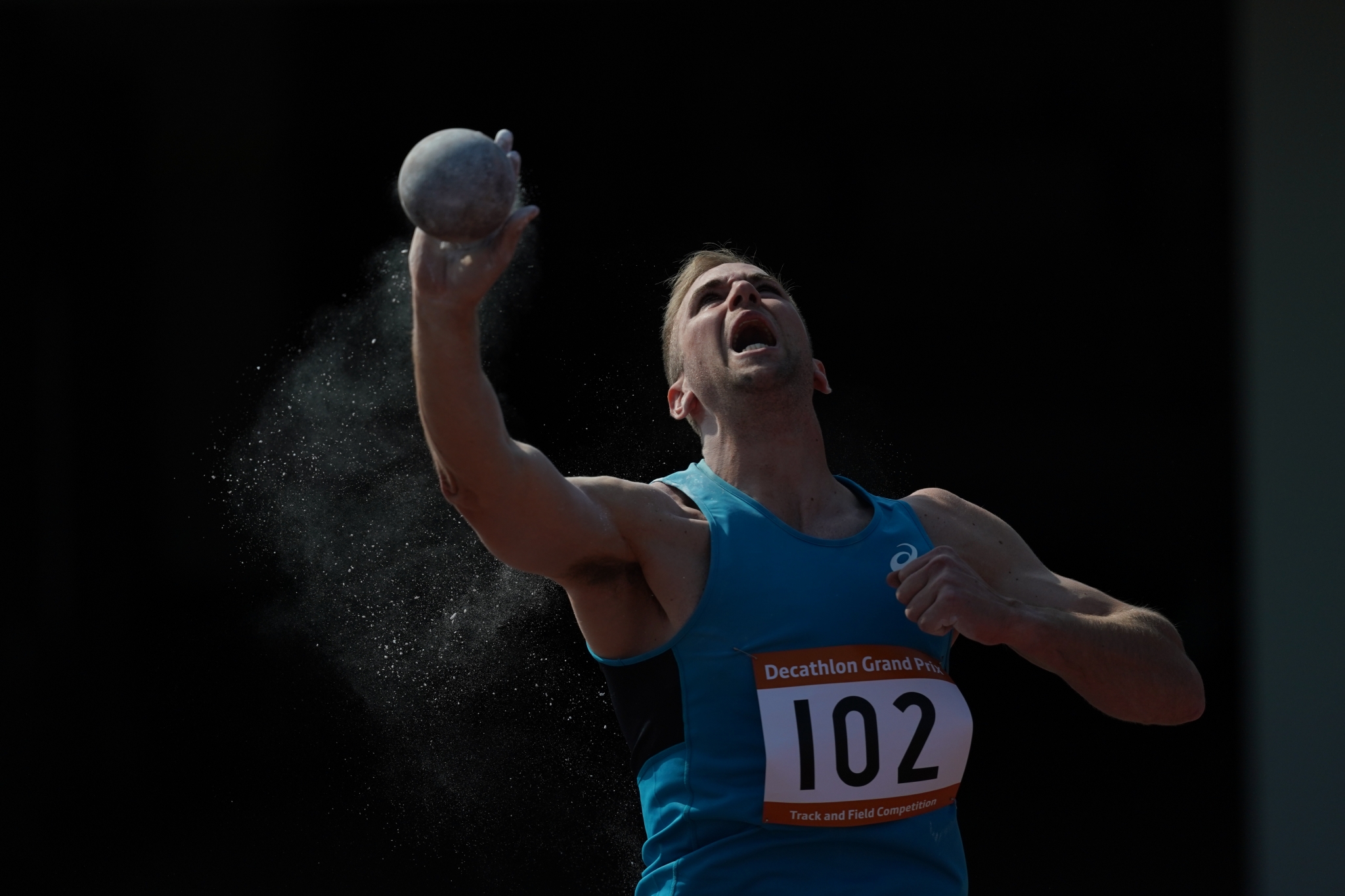 Male athlete throwing shotput, arm raised as he releases the ball