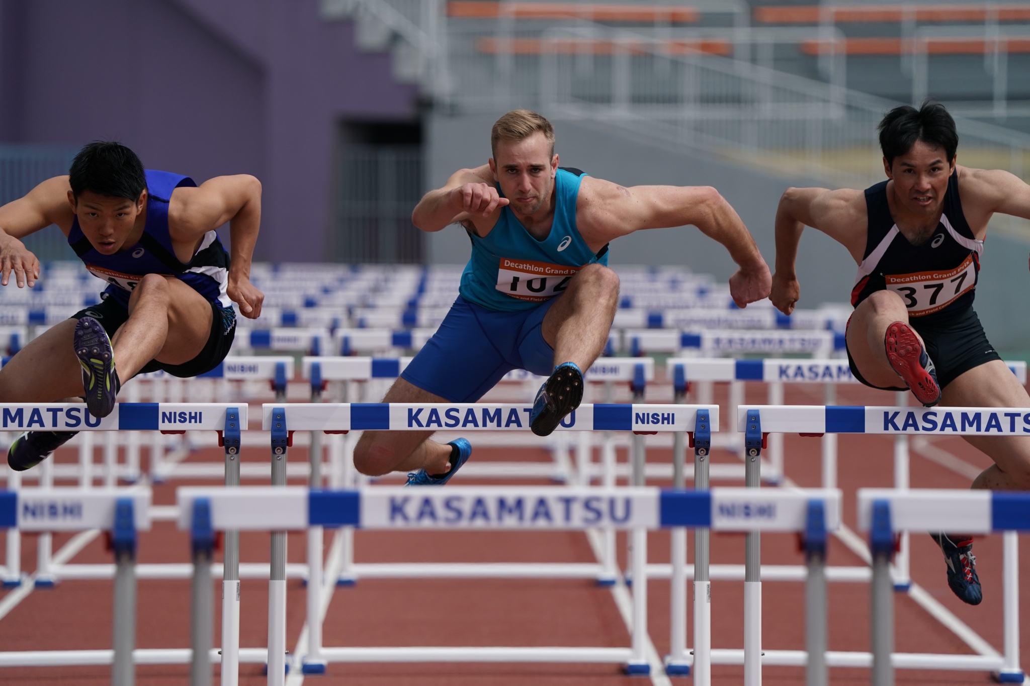 Three male athletes racing over hurdles