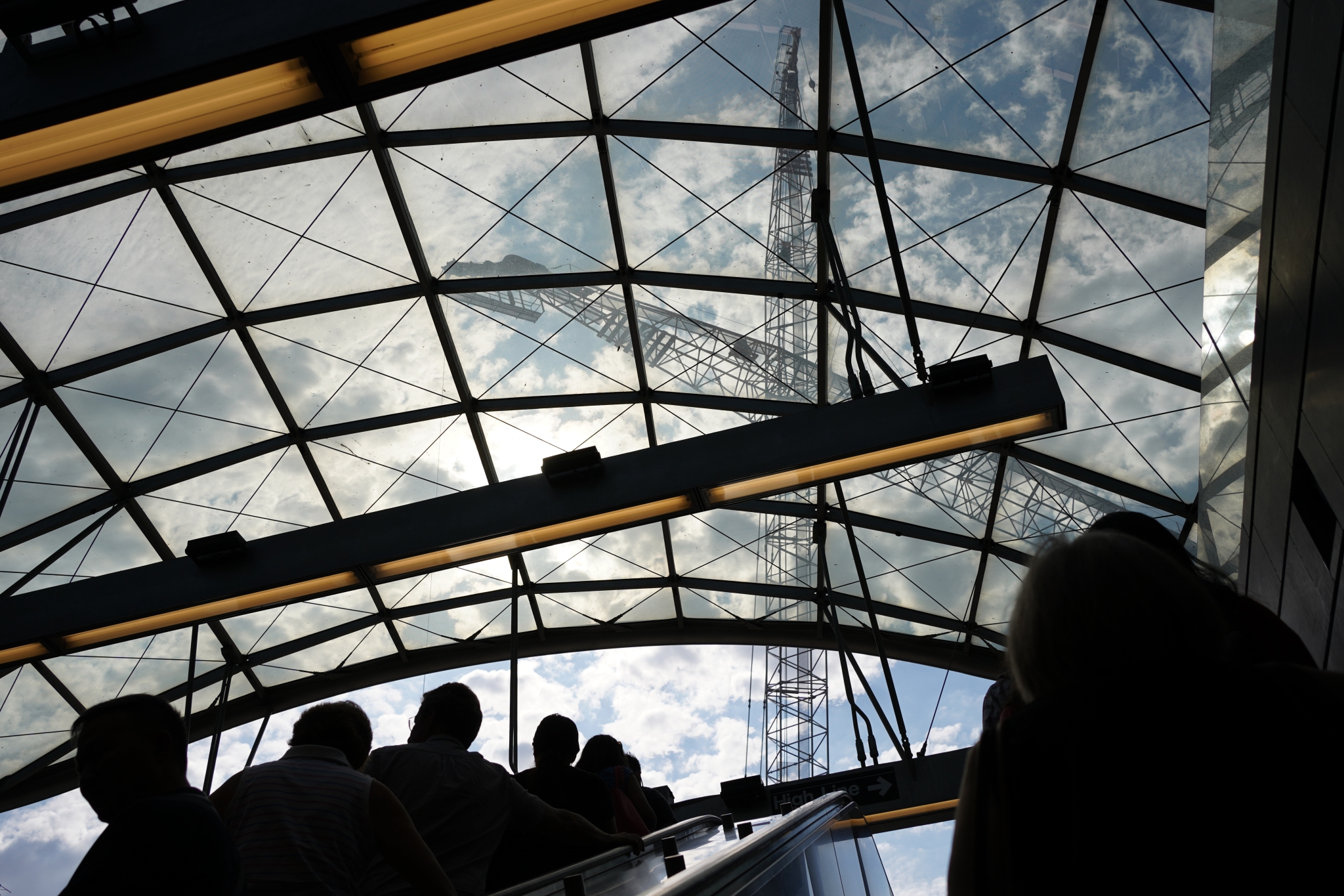 A large curved glass roof over silhouetted people riding an escalator