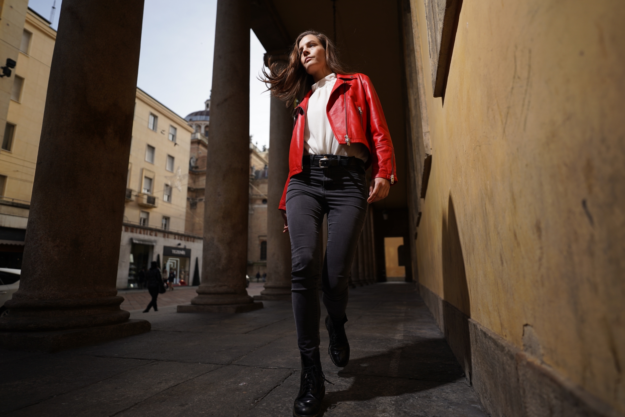 Female model in red jacket walking next to a building with columns
