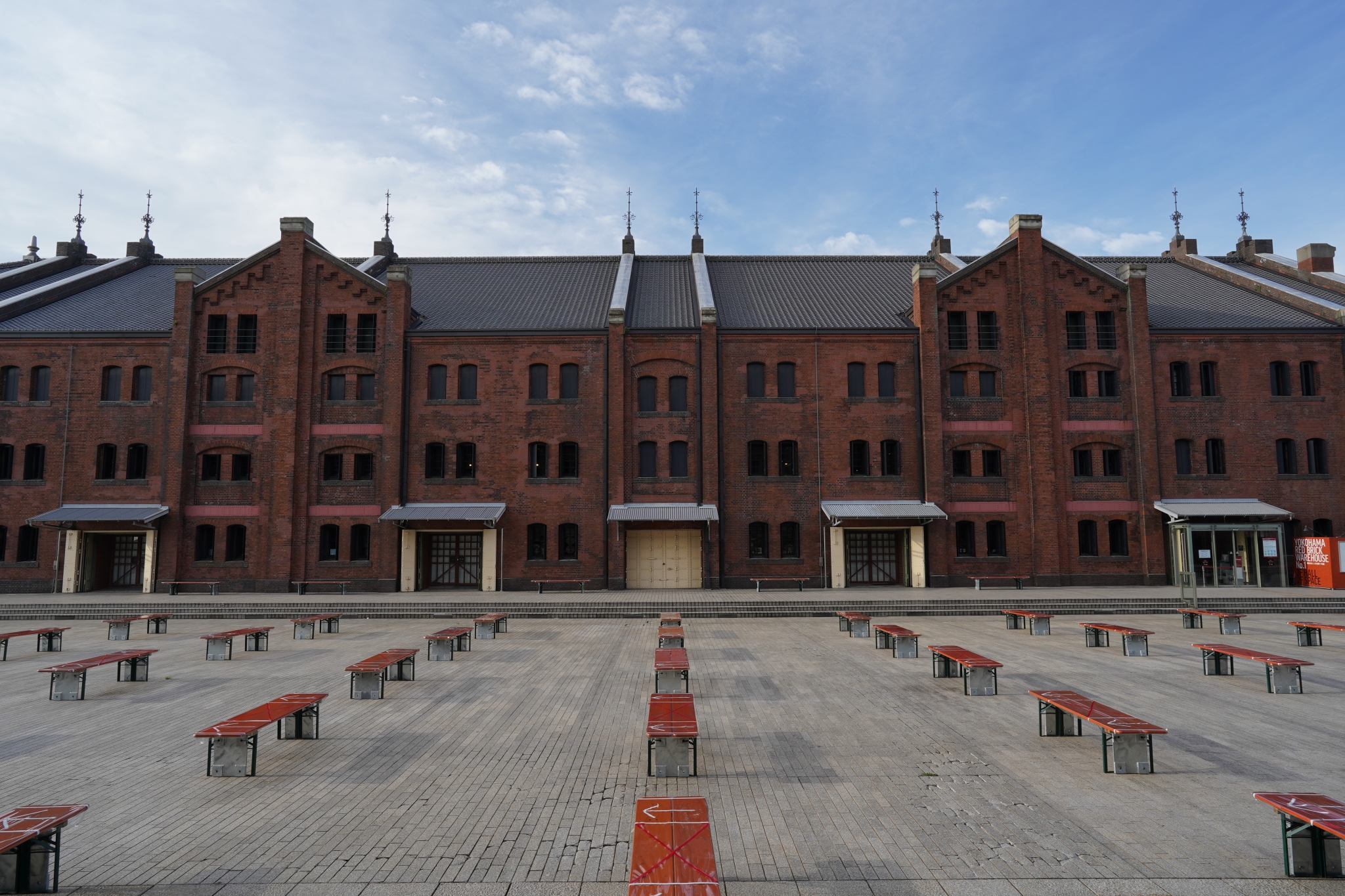 Wide red brick building and benches laid out systematically in front of it