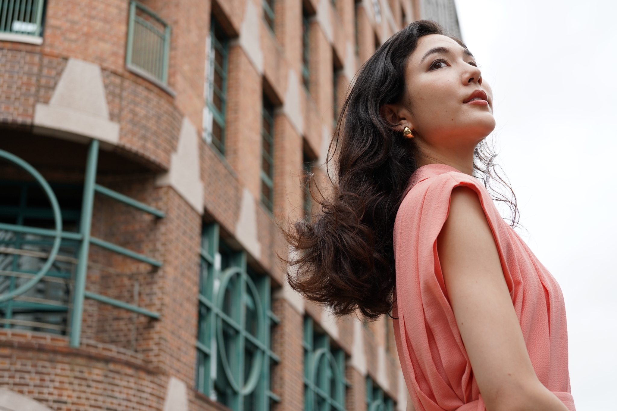 Female model stood to the right of the frame with a brick building in the background