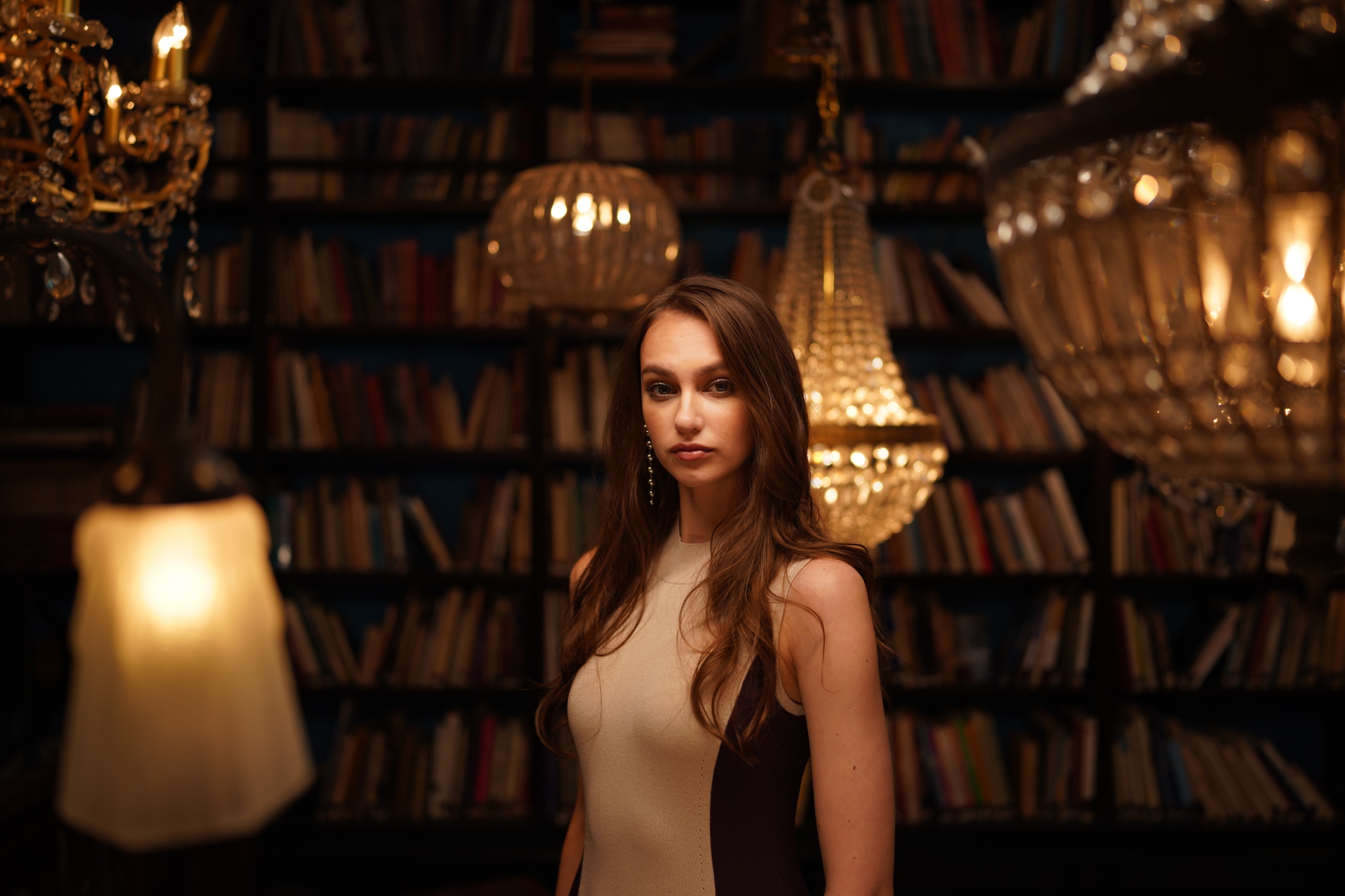 Female model in a dimly lit room with hanging lights and bookshelves