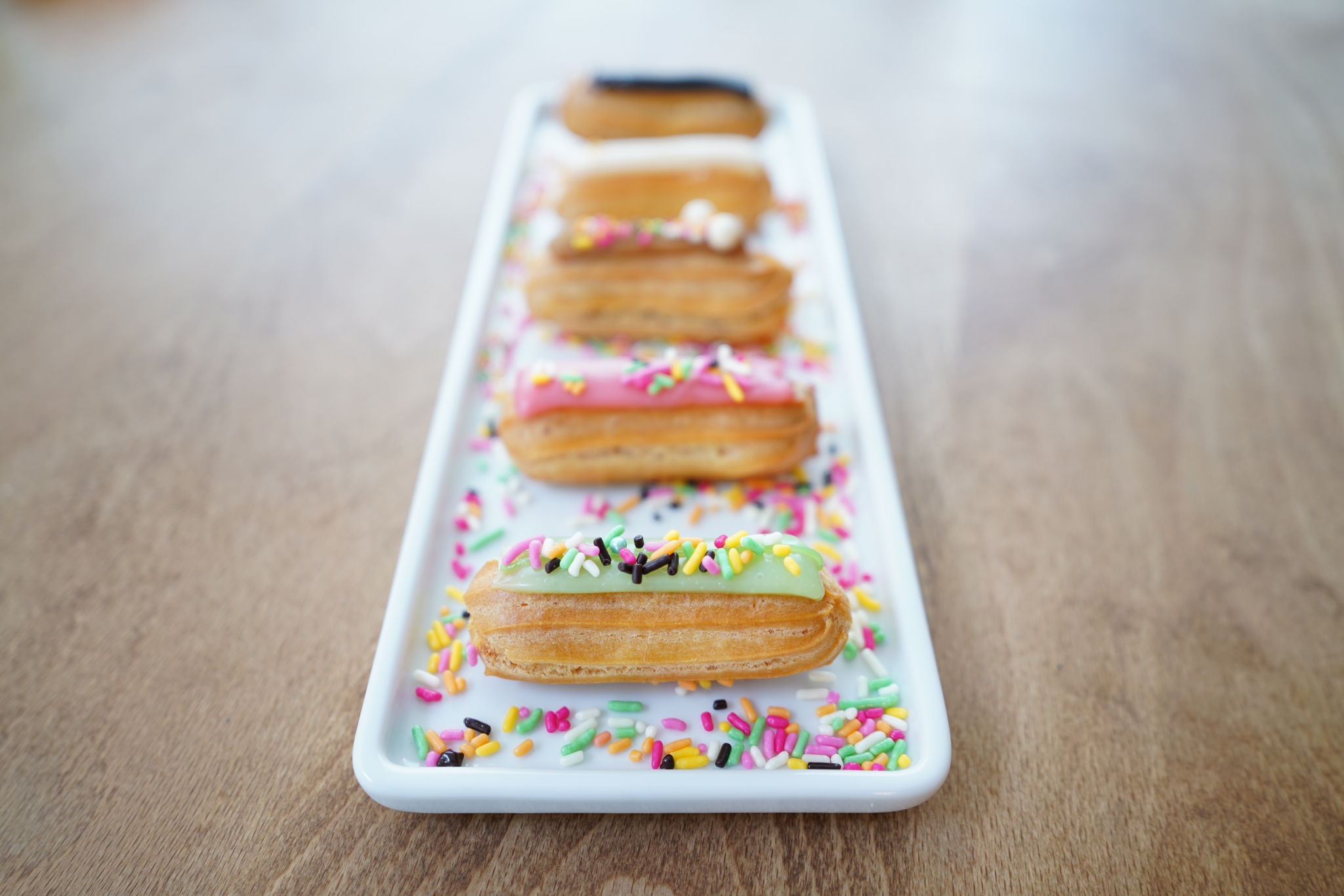 Colourful eclairs lined up on plate with bokeh background