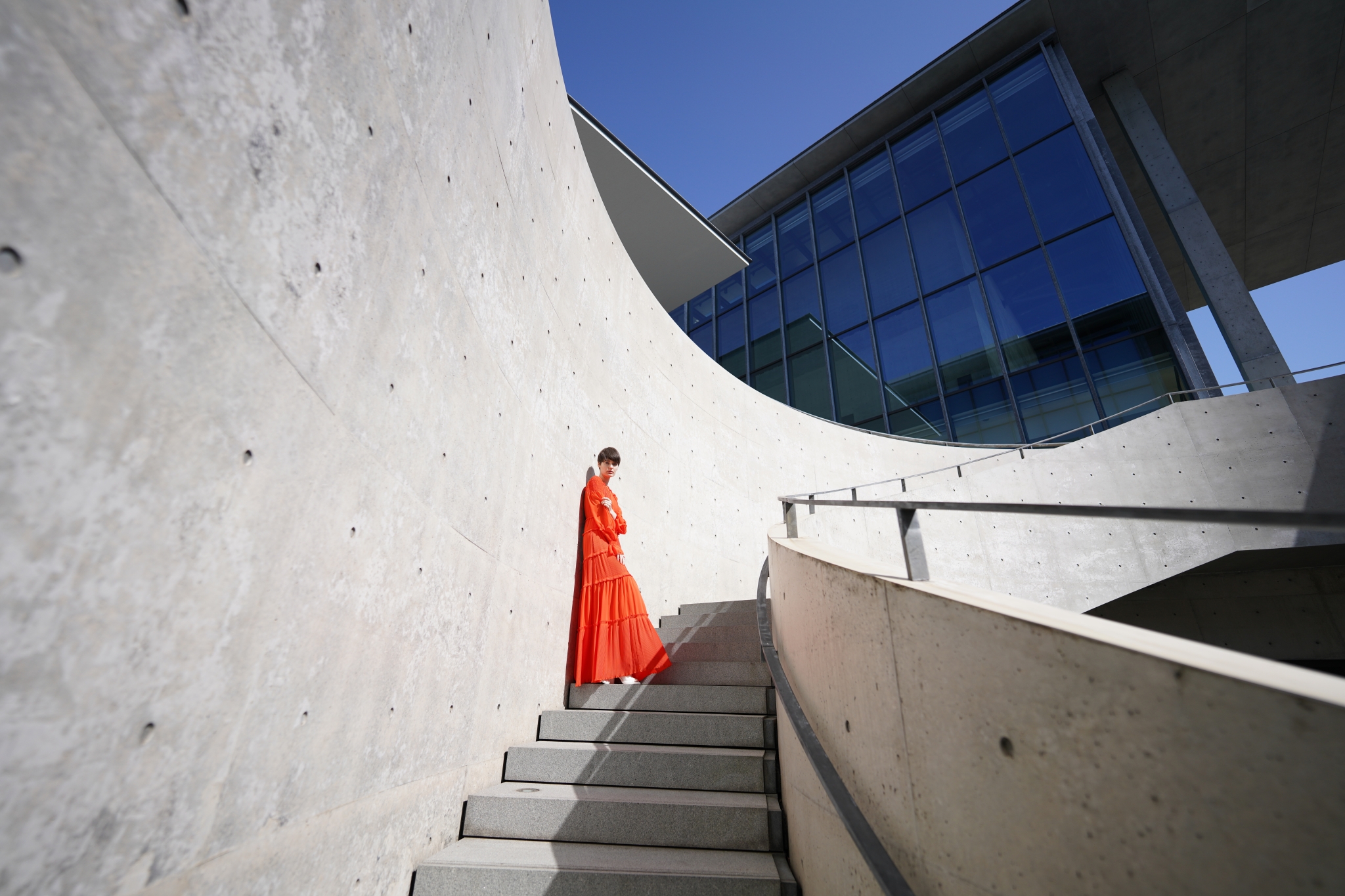Wide shot of female model stood on a concrete staircase leading to a tall glass building