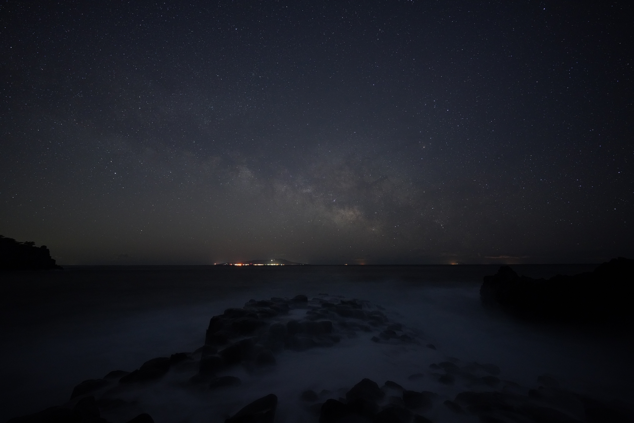 A rocky coastline at night-time with the lights of settlement in the distance