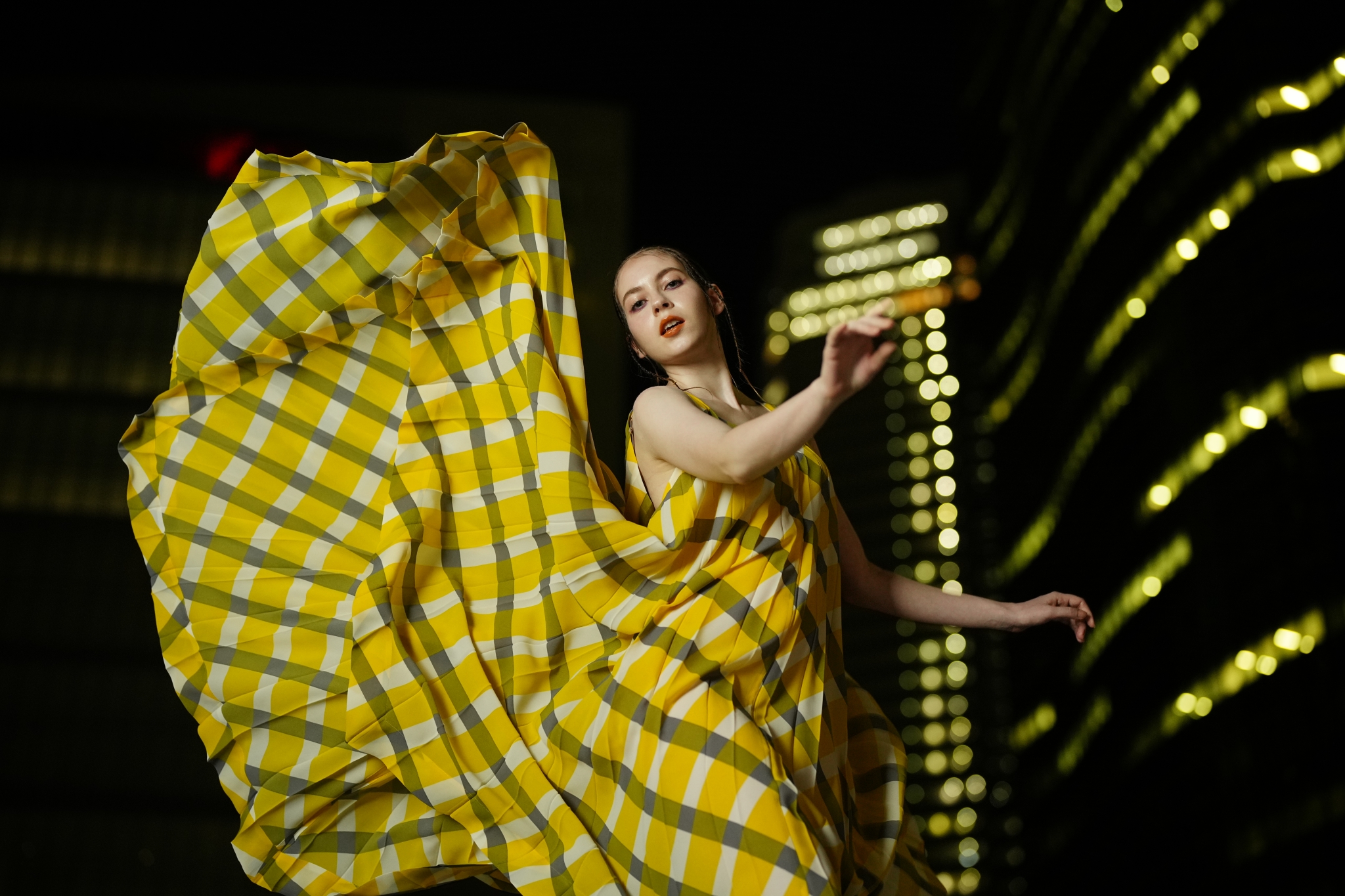Female model at night wearing a yellow billowy dress with a tall building in the background