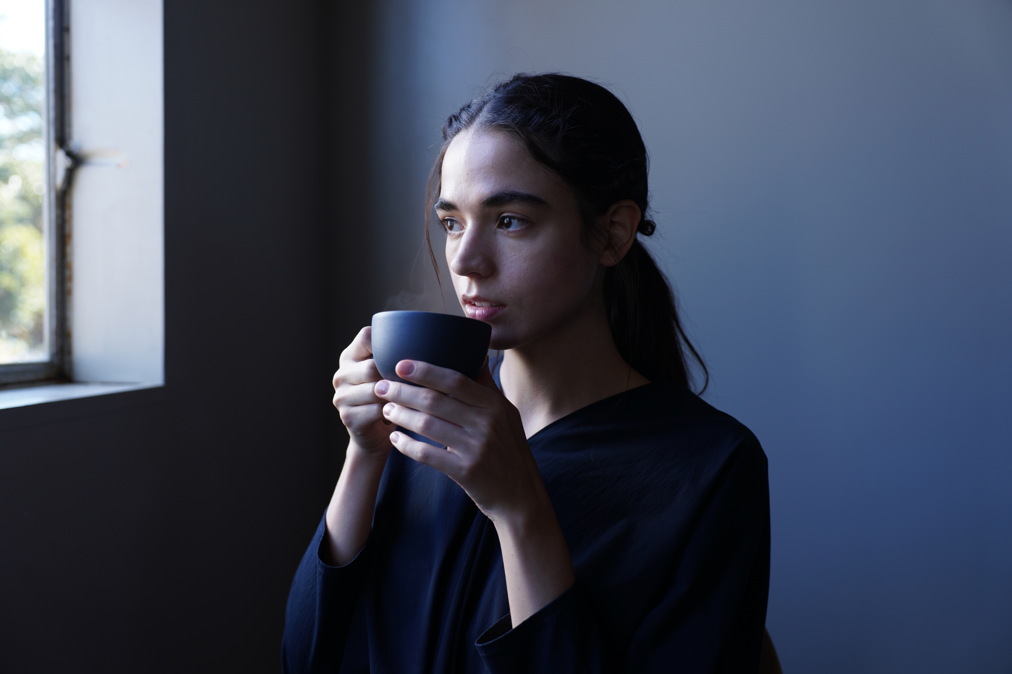 Female model sipping a cup of tea looking towards a window