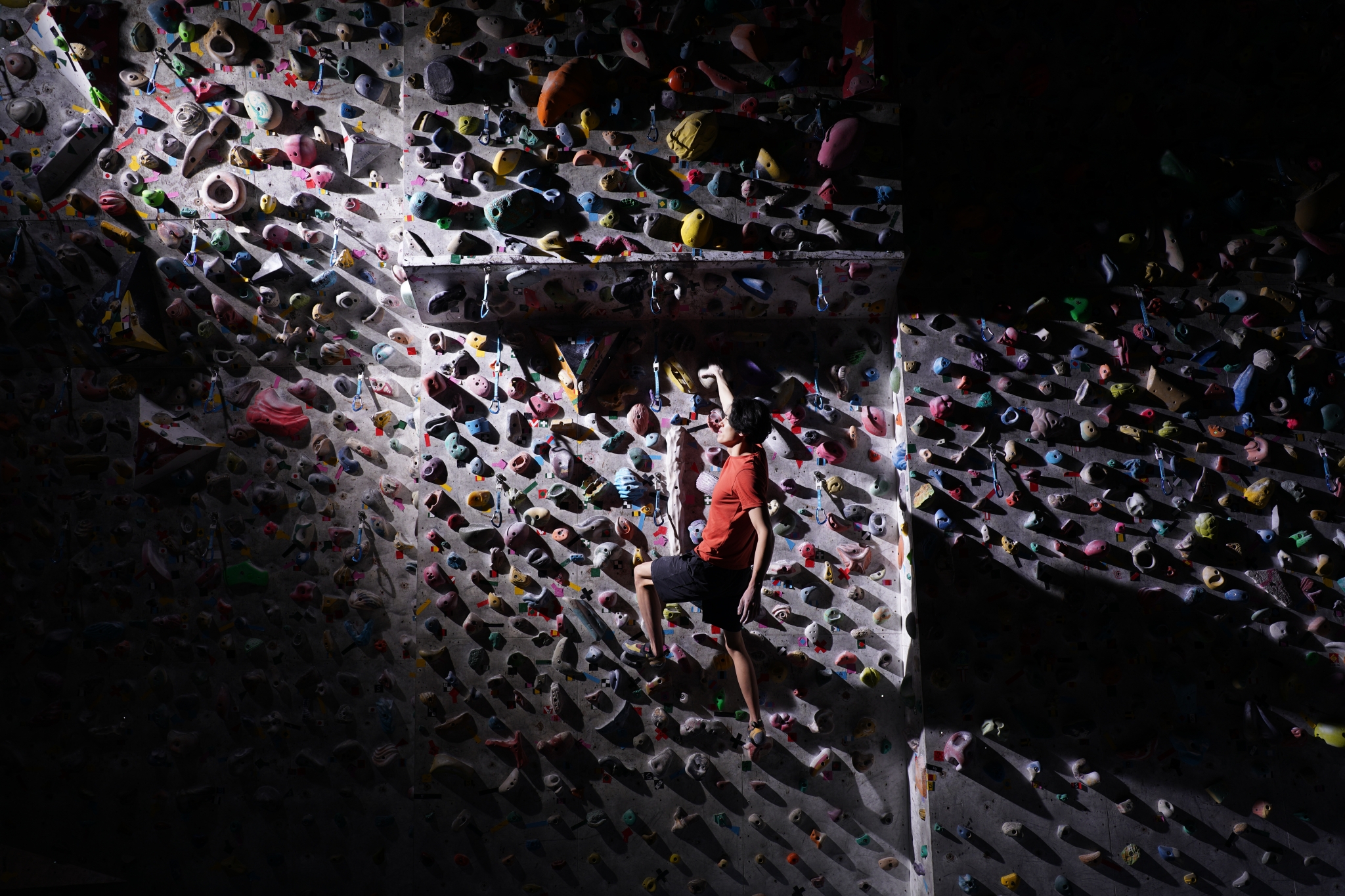 Man at a bouldering gym climbing a wall, lit by a ray of light 