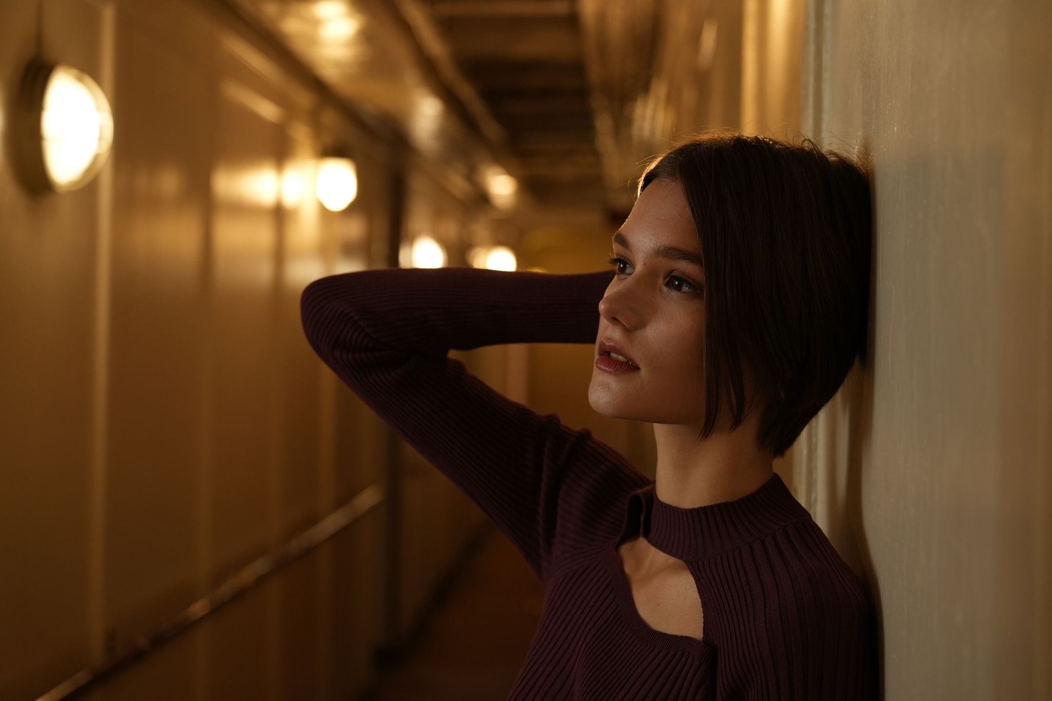 Female model in a dimly lit corridor, arm raised to her face