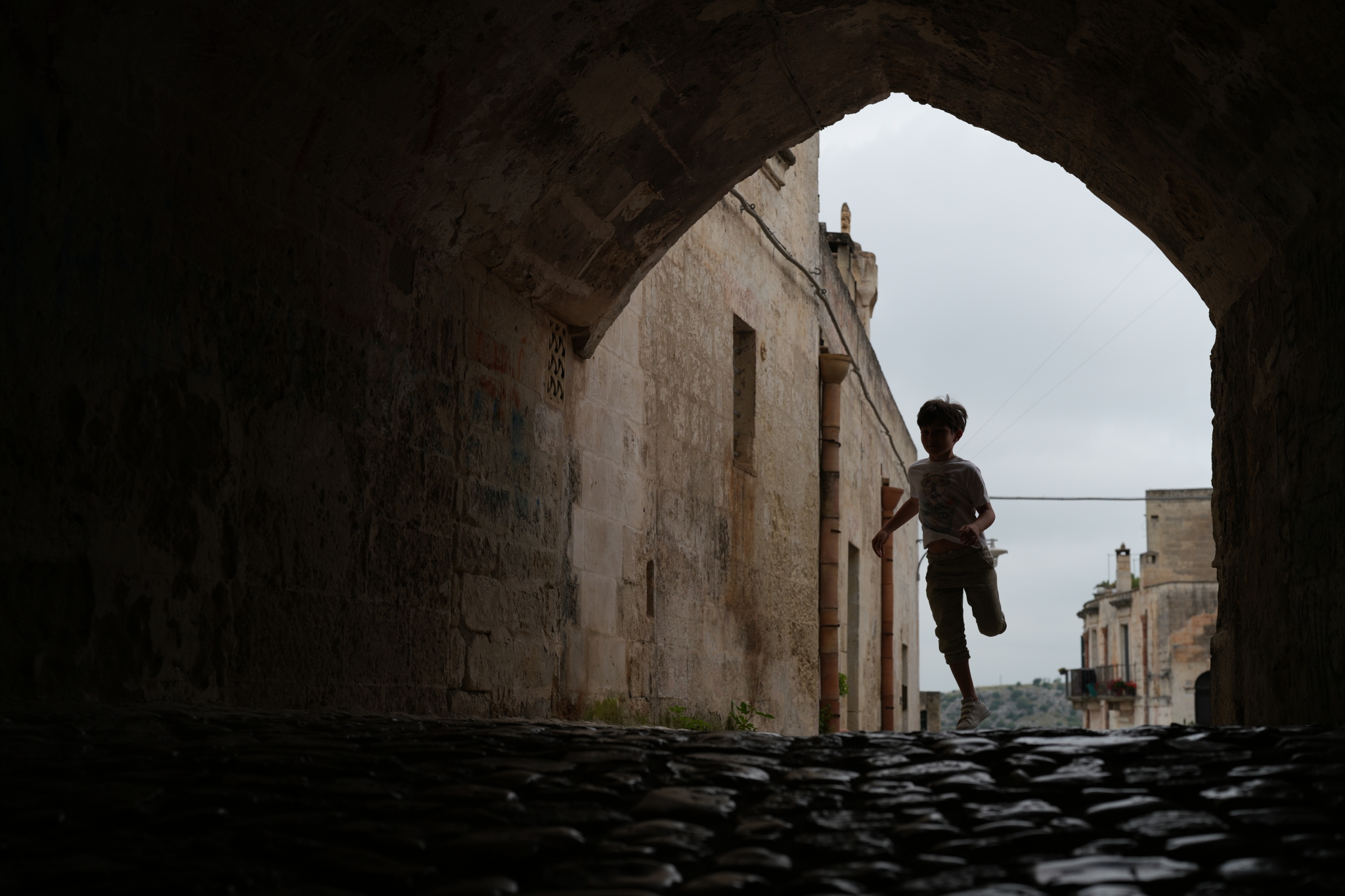 Young boy running through an archway, silhouetted against the sky