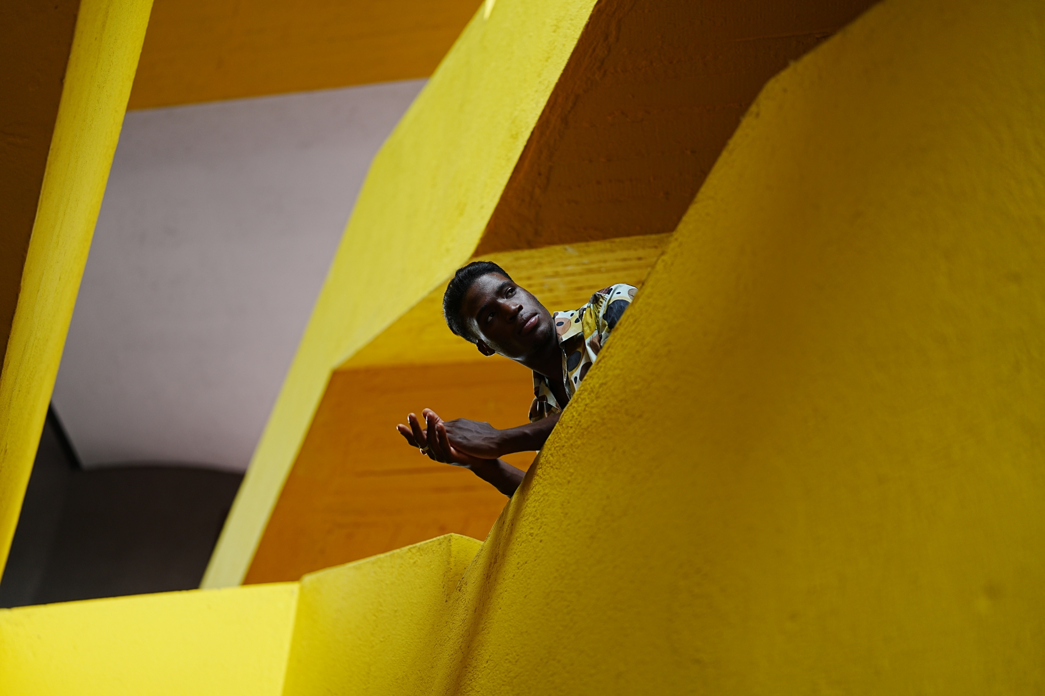 Male model leaning over the balcony of a yellow building