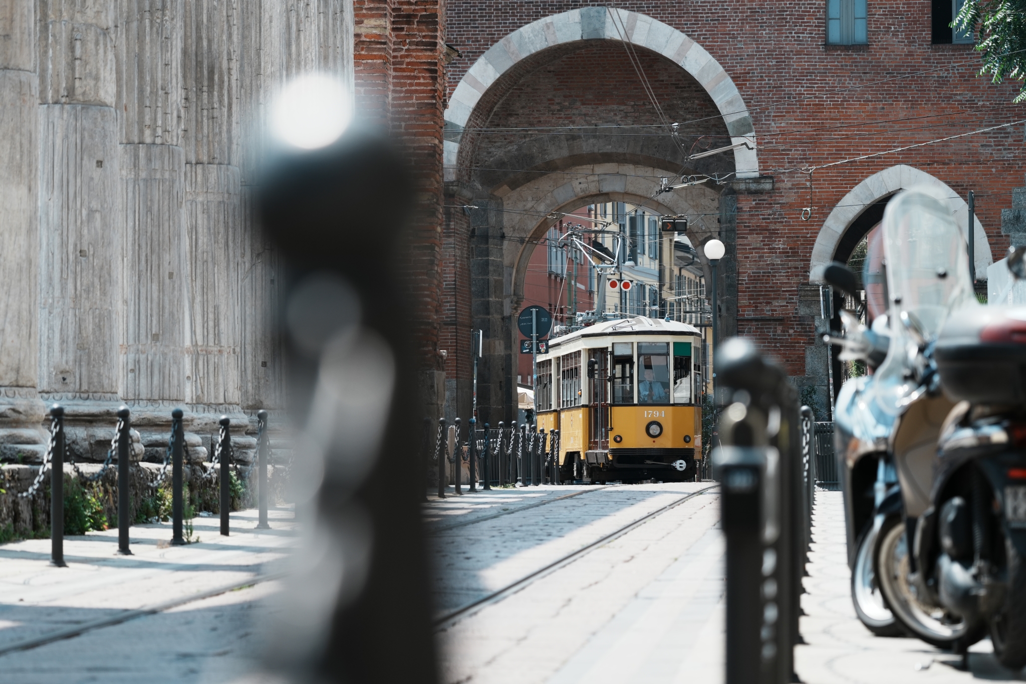Tram travelling through an archway with a bollard in bokeh foreground