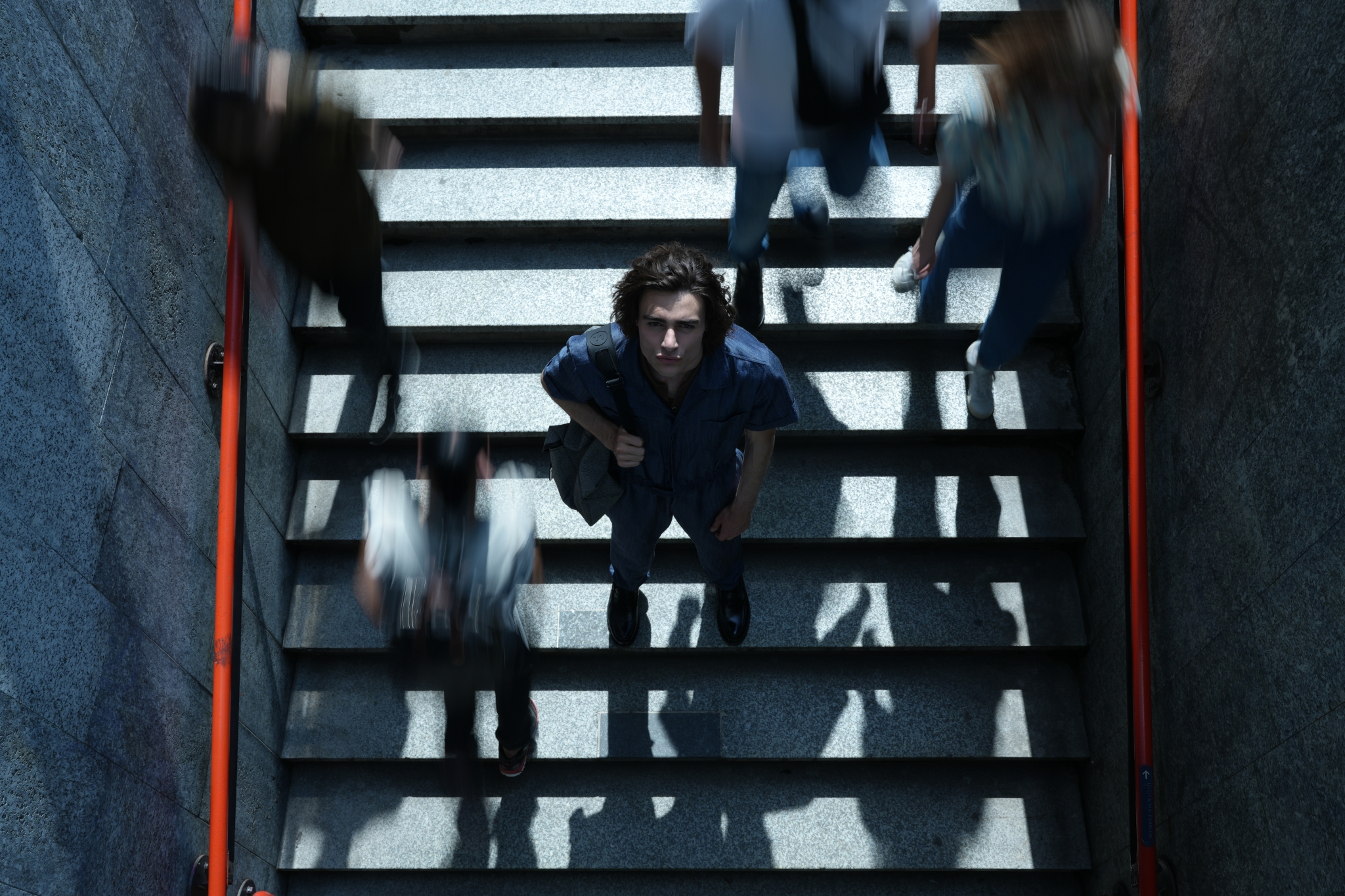 Aerial shot of male model stood on a staircase looking upward as people pass by