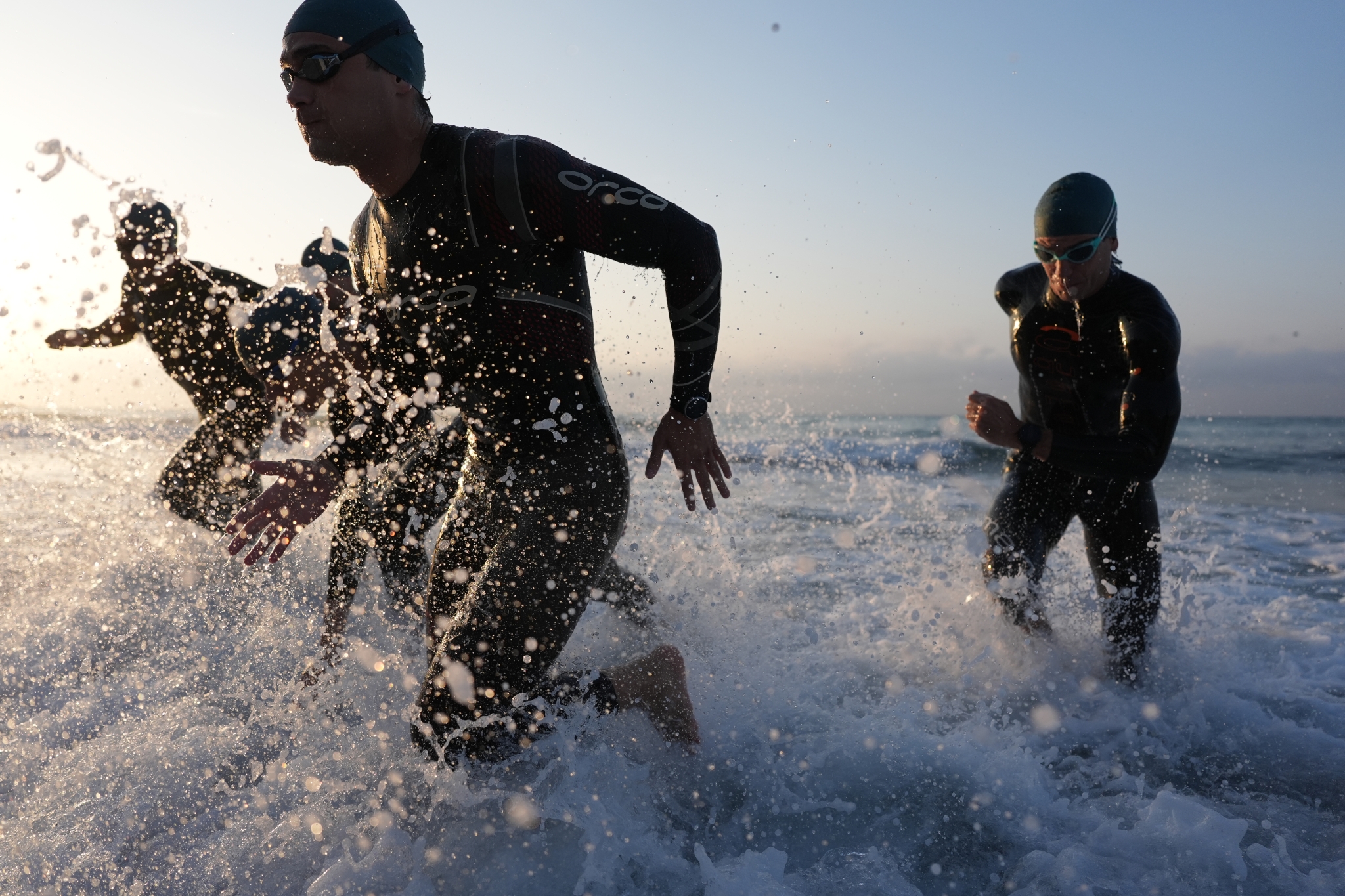 Male athletes running into the sea as waves spray around them