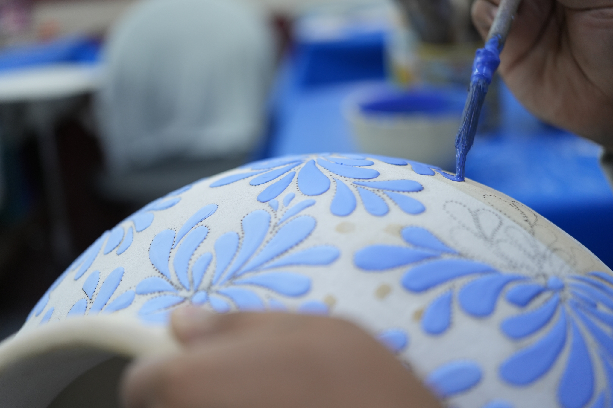 Close-up of a paint brush applying cornflower blue paint to a white jar