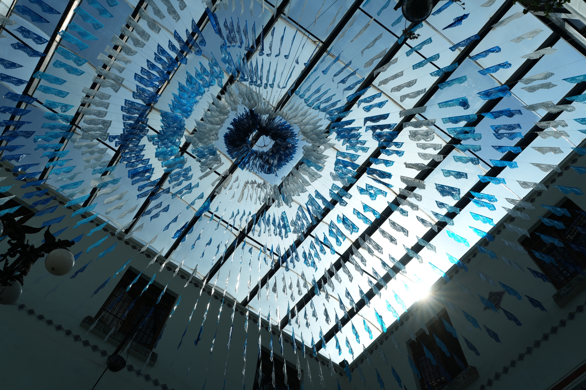 A square glass ceiling decorated with semi-translucent flags, illuminated by the sun