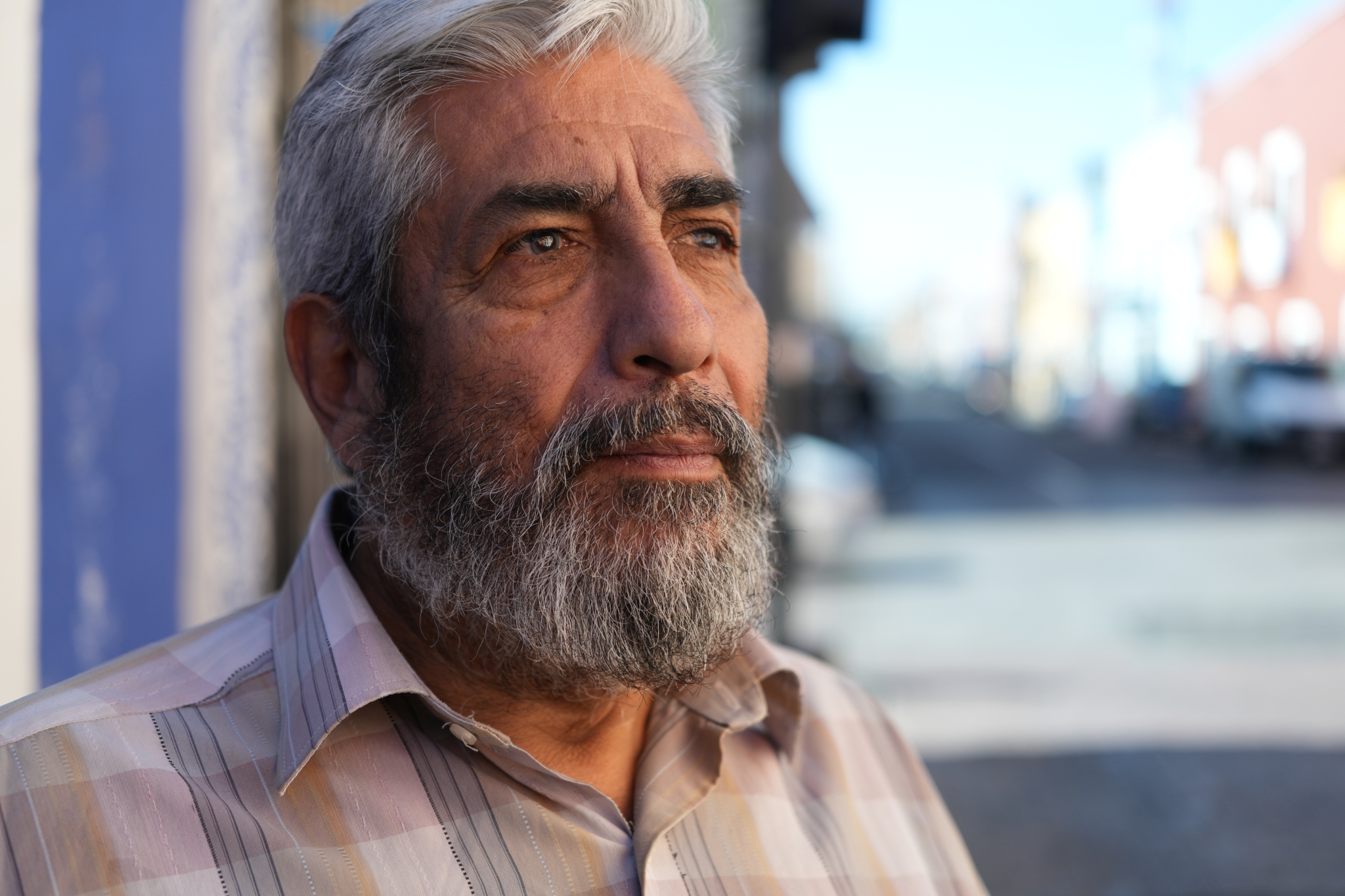 Portrait of a mature bearded male model looking to the right, with a row of buildings in a bokeh background