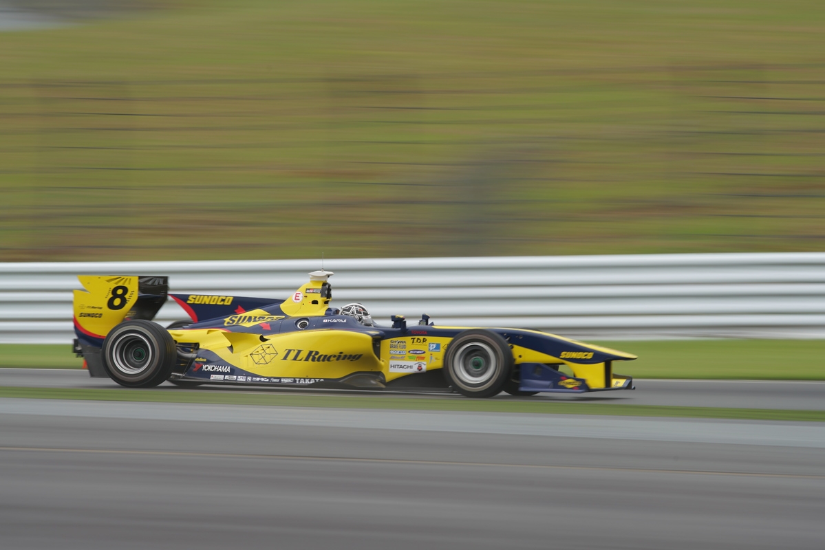 Side view of yellow racing car on track, with motion blur on track and background
