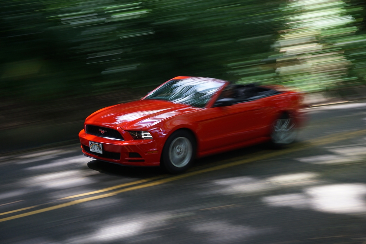 Open-top red car in motion, with motion blur on road and background foliage
