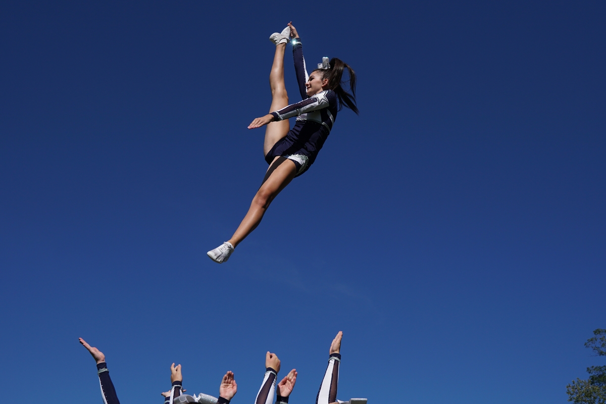 Cheerleader striking a pose in mid-air with teammates below