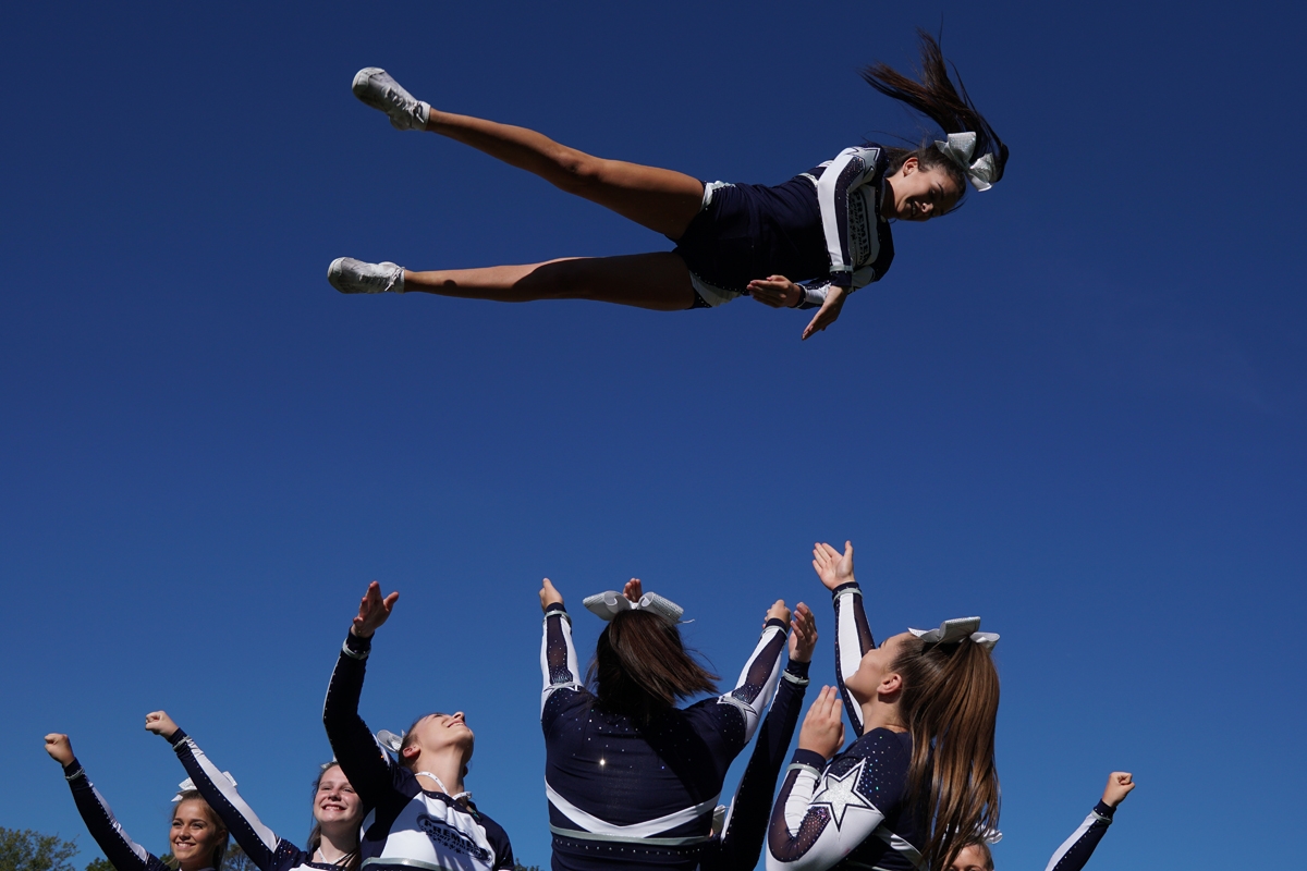 Cheerleader horizontal in mid-air with teammates below
