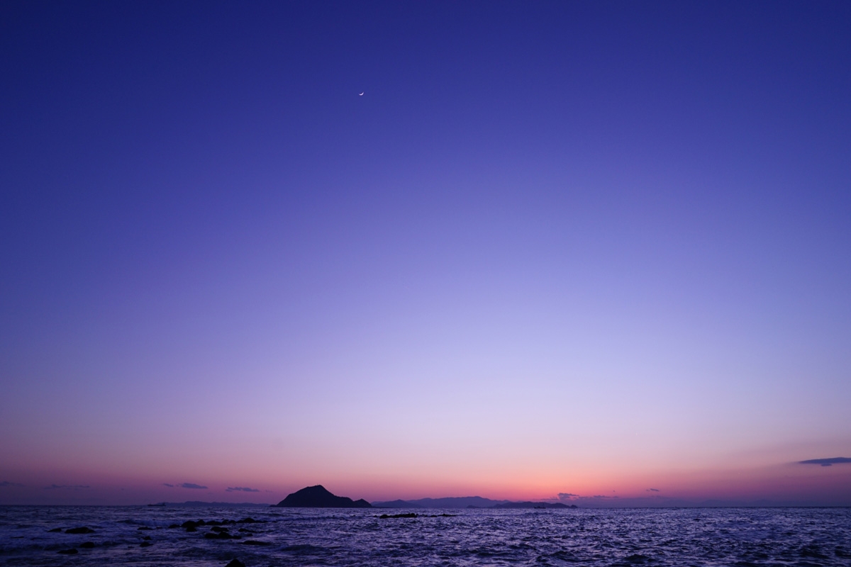 Wide shot of ocean with island and red post-sunset sky