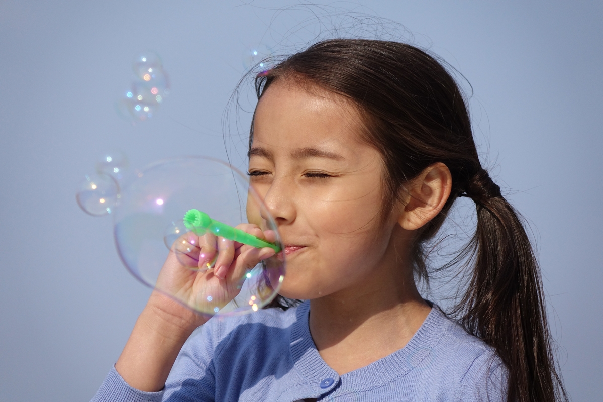 Semi-profile portrait of girl blowing bubbles with a pipe