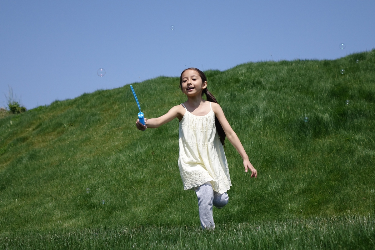 Girl running on grass chasing bubbles