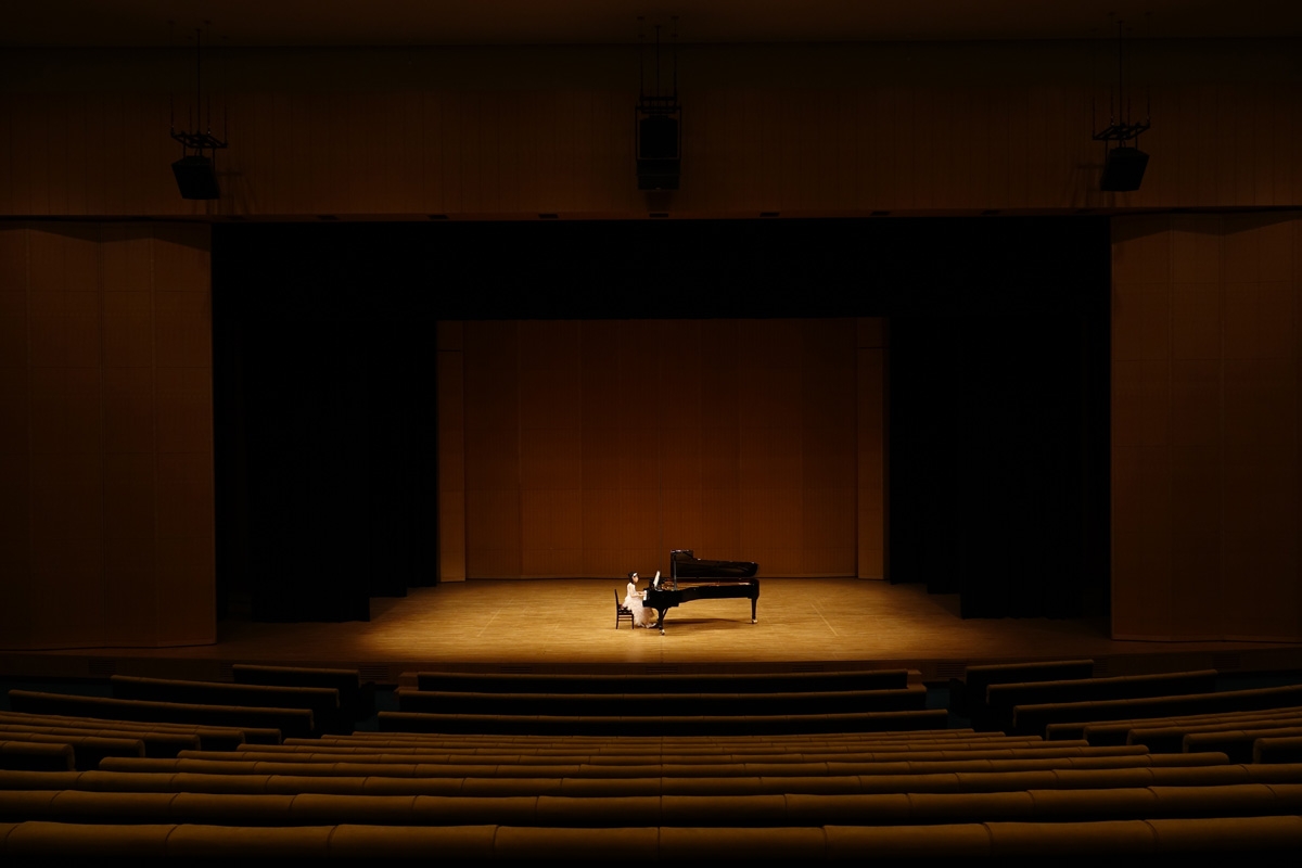 Long and wide shot of woman playing grand piano on stage in concert hall